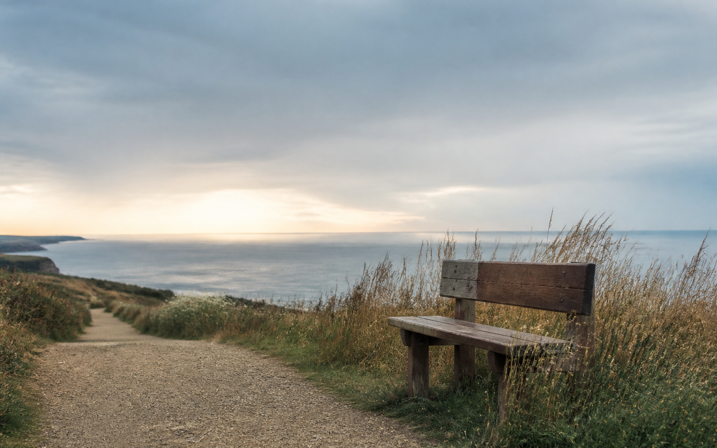 A quiet coastal path leading past a wooden bench toward an open horizon