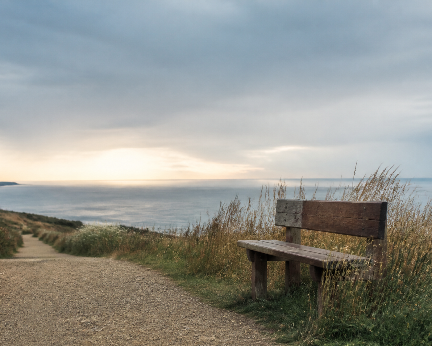 A quiet coastal path leading past a wooden bench toward an open horizon