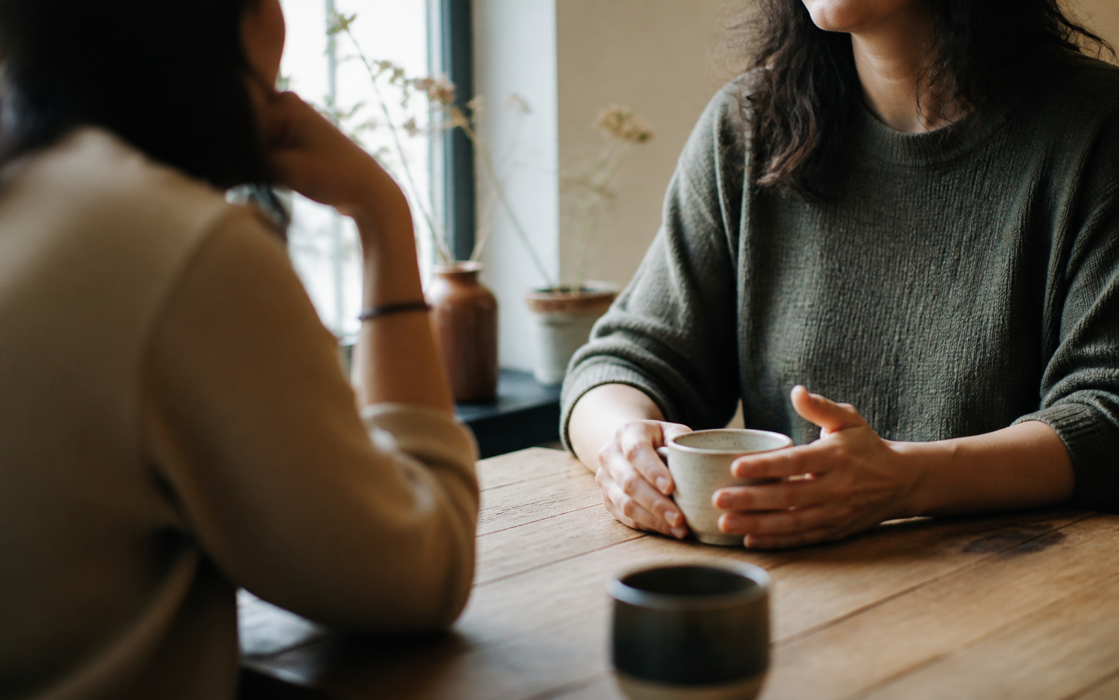 Two adults having a thoughtful conversation over coffee at a warm wooden table