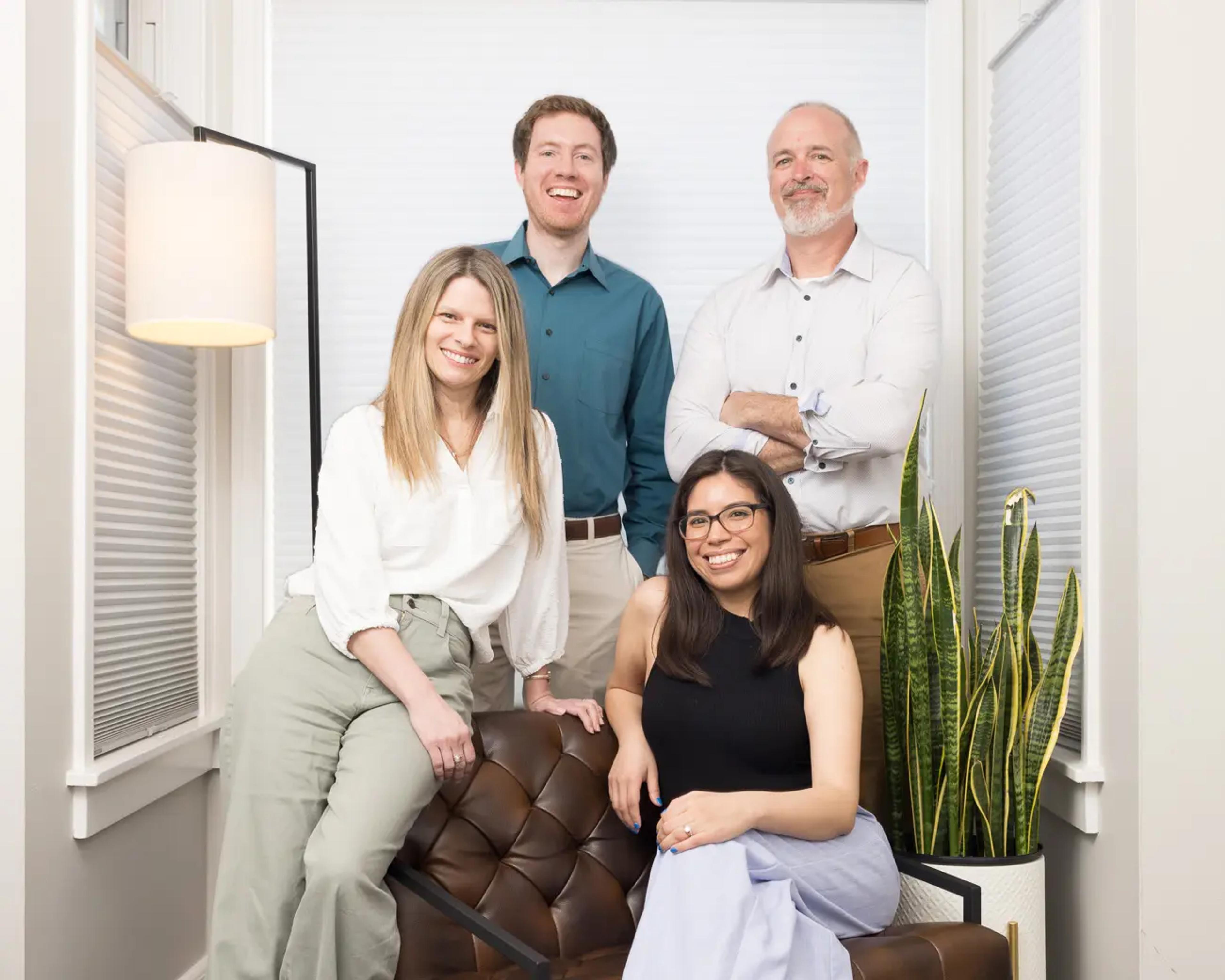 Four smiling professionals, two men and two women, in a modern office setting.