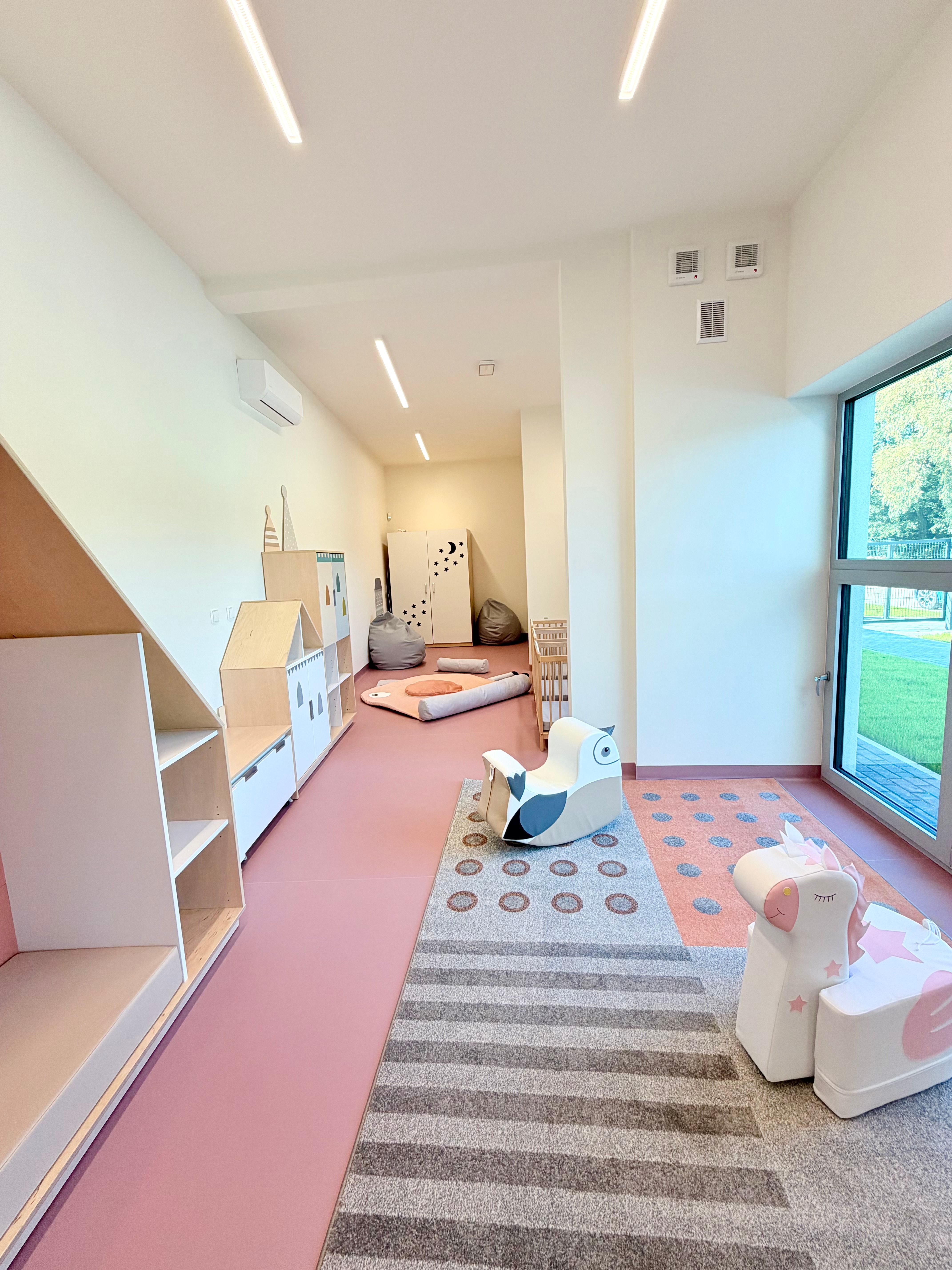 Sala Małych Kroków — jasna sala z meblami w kształcie domków, miękkimi siedziskami i dużym oknem