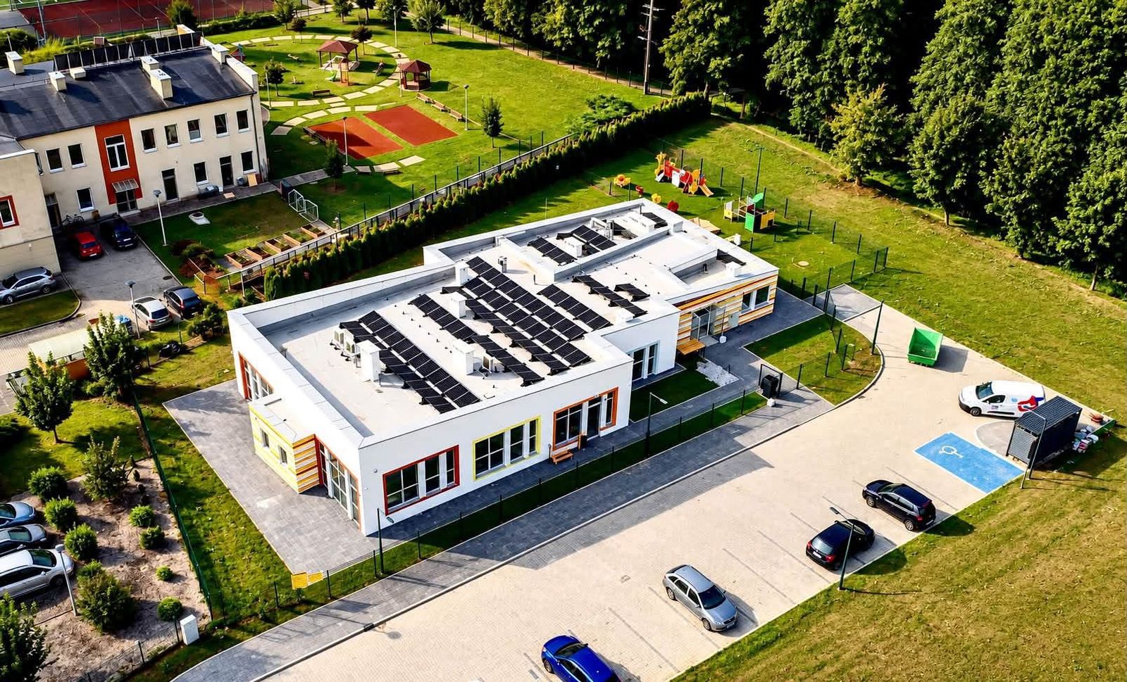Budynek żłobka z lotu ptaka, obok plac zabaw i parking