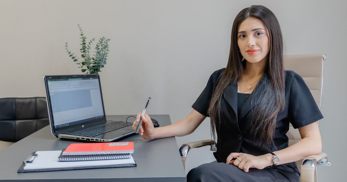 A woman sits at a desk with a laptop.