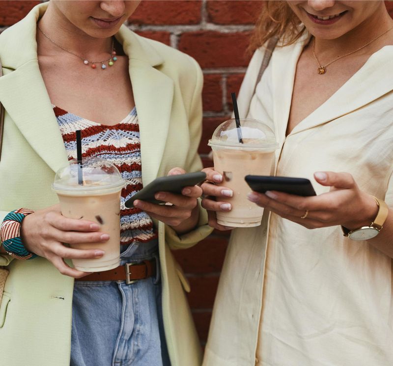 2 friends drinking ice coffee look at the Credit Building feature in-app