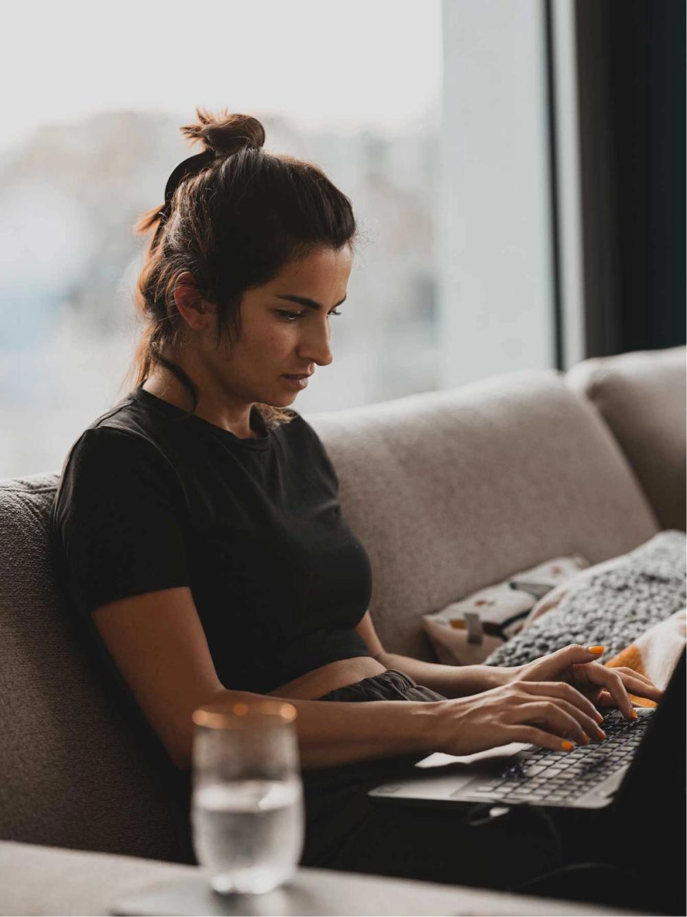Une femme sur un canapé rédige un avis sur KOHO sur son ordinateur, soulignant l'impact positif du renforcement de crédit sur ses scores