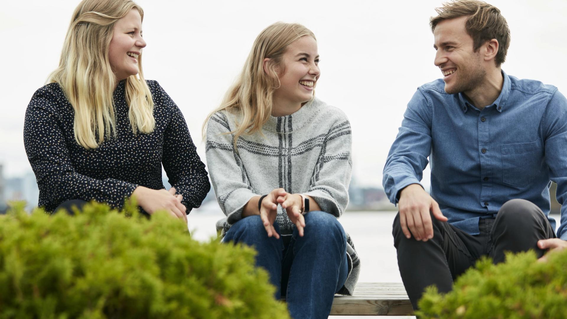 Two blond women and a brown-haired man sitting on a bench and chatting.