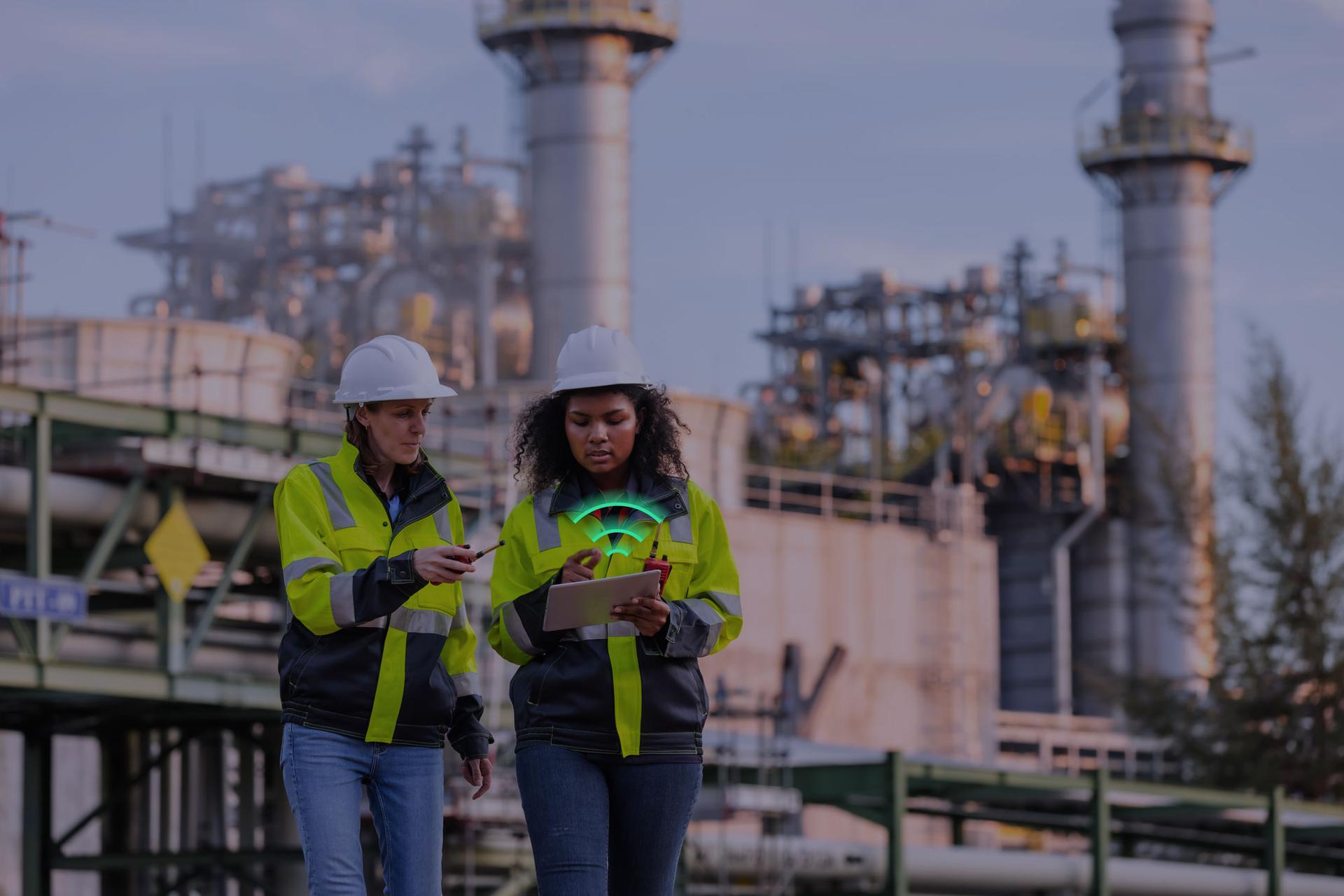 Two women in reflective jackets and hardhats looking at a tablet