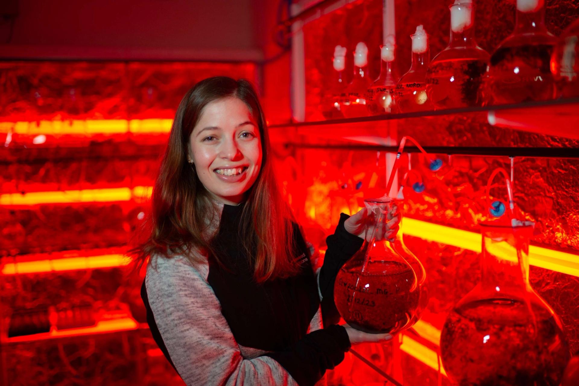 female biotechnologist holding a beaker in a red-lit lab