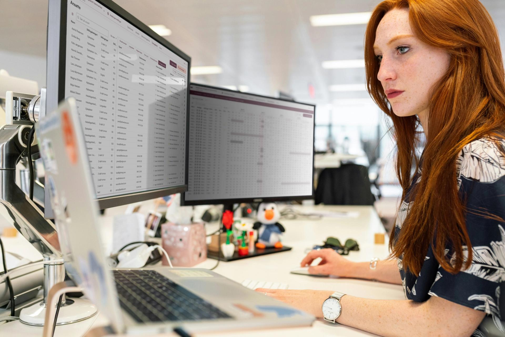 Red-headed woman at a desk in front of two screens