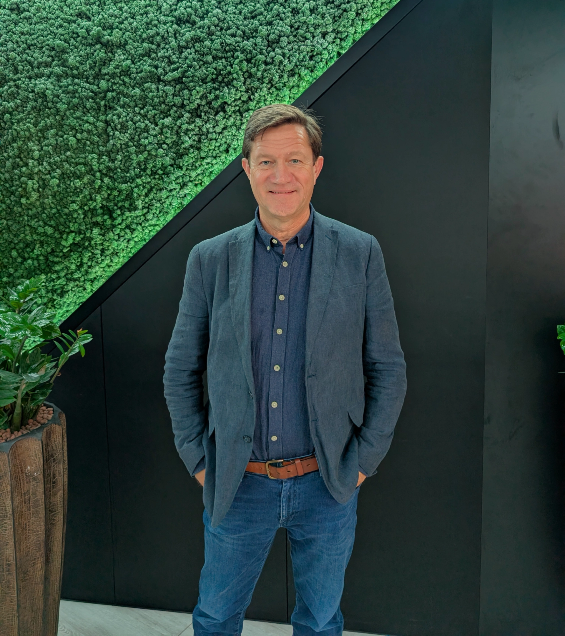 Man in a blue button up shirt, blue linen blazer and blue jeans against a black backgeround