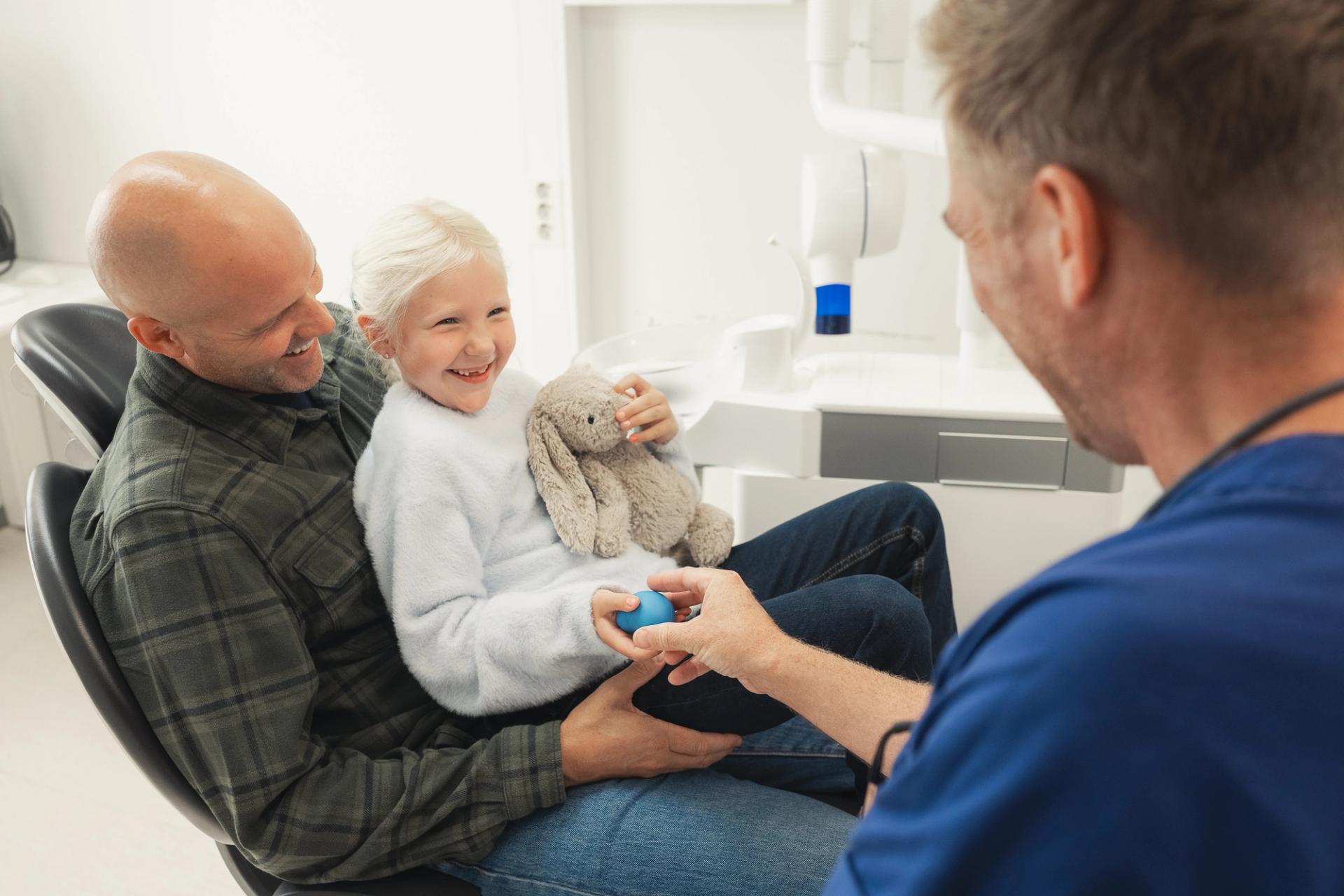 A father and his daughter at the dentist office, smiling and happy.