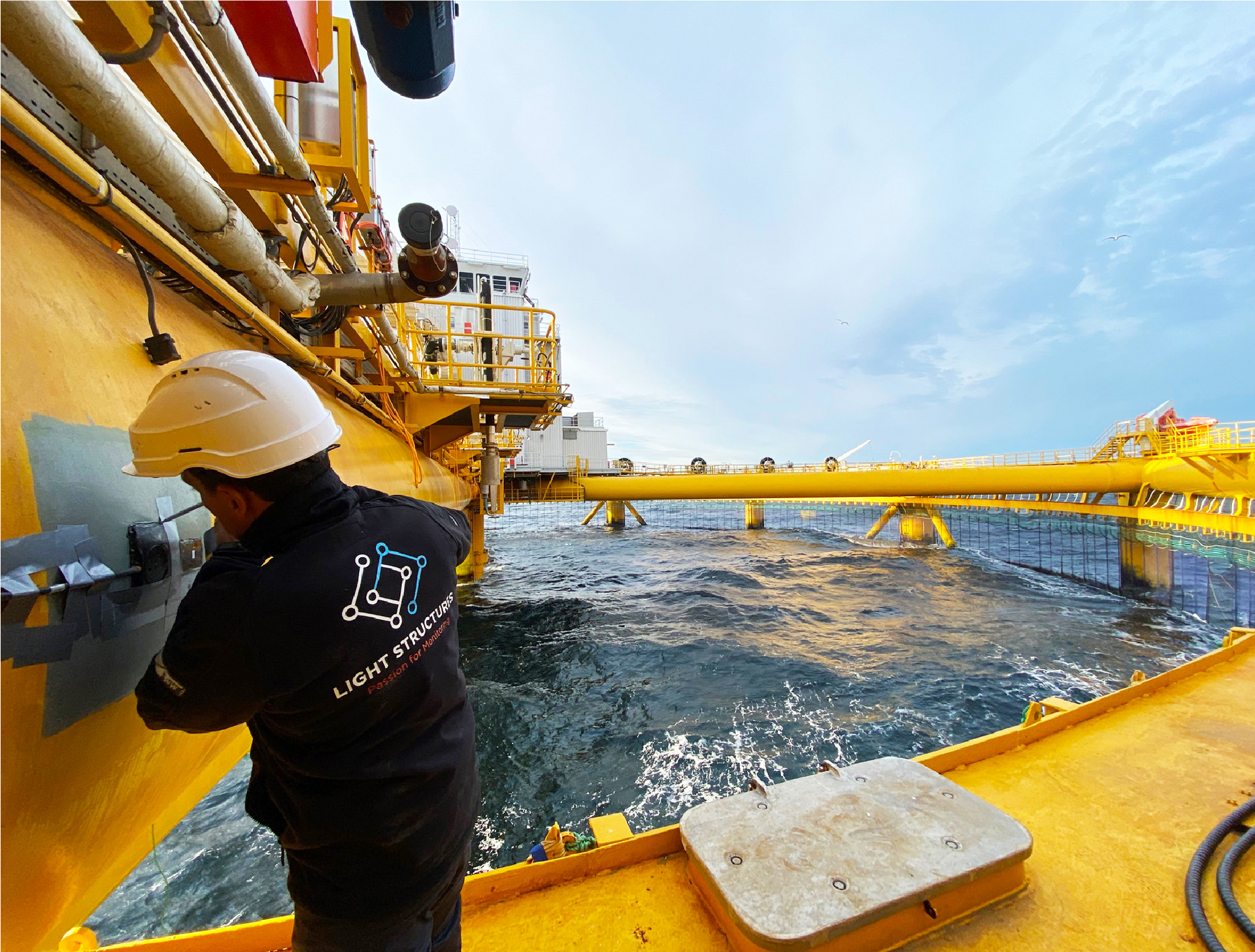 Man in a hard hat working on a yellow fish farm at sea