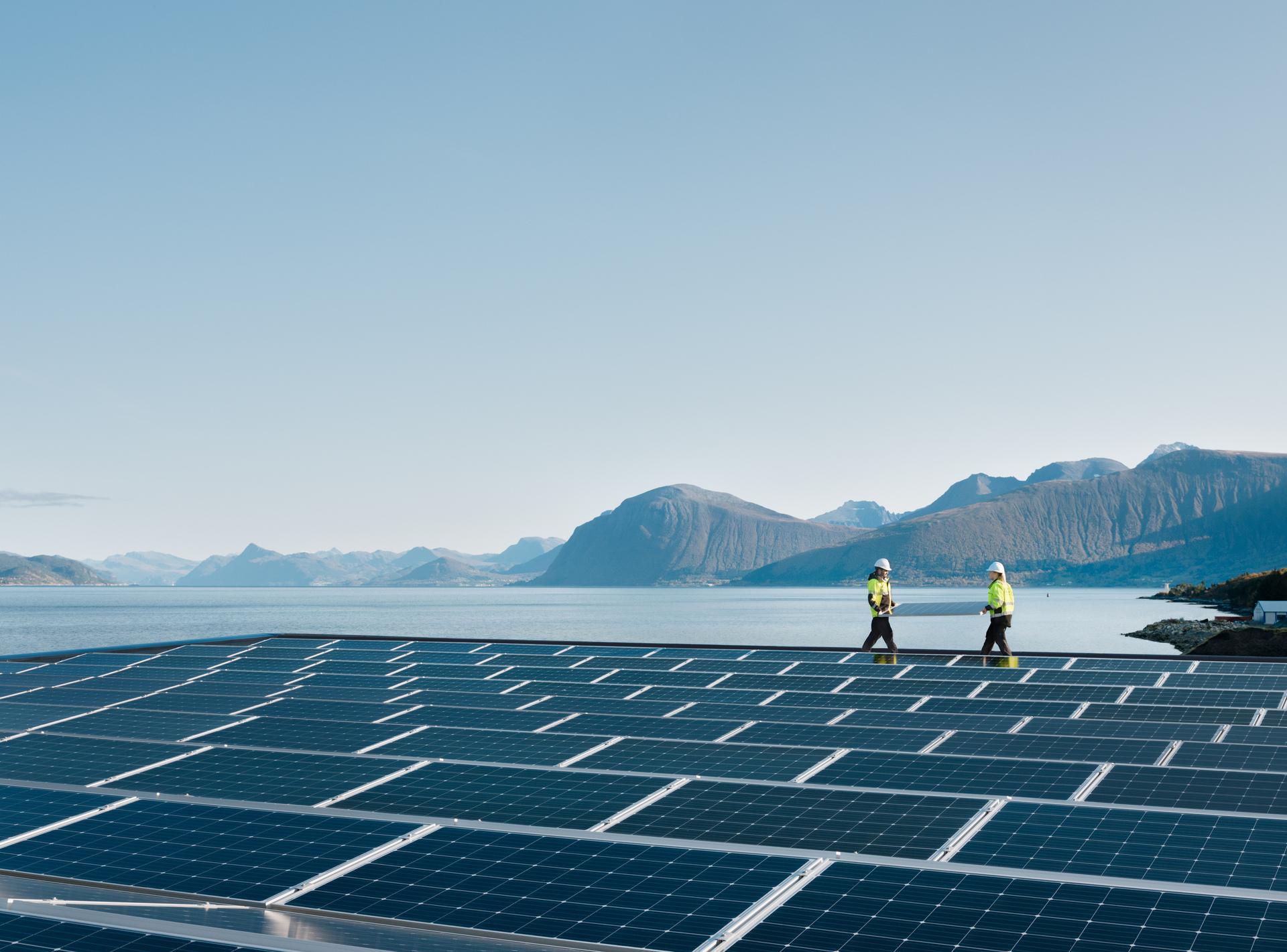 Two workers installing solar panels with mountains in the background