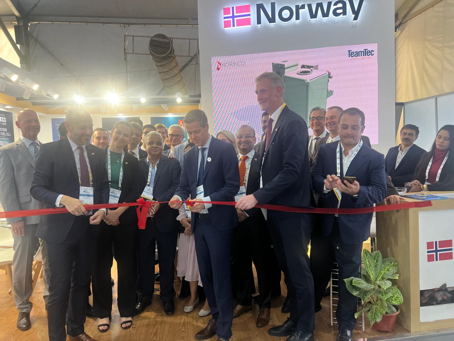 A group of people cutting a red band at a Norwegian pavilion