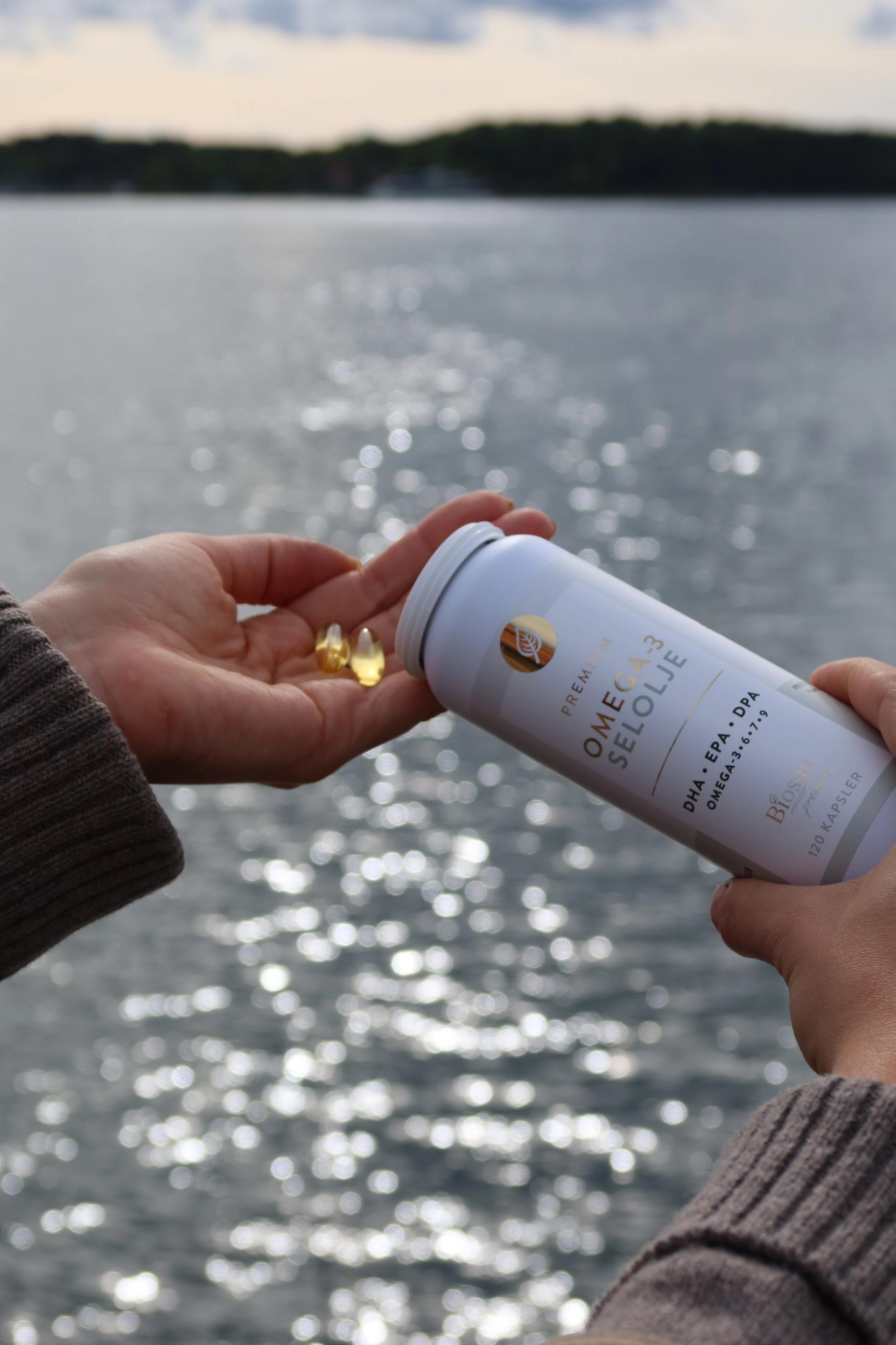 Hands pouring golden supplement capsules from a white bottle, with sparkling water behind