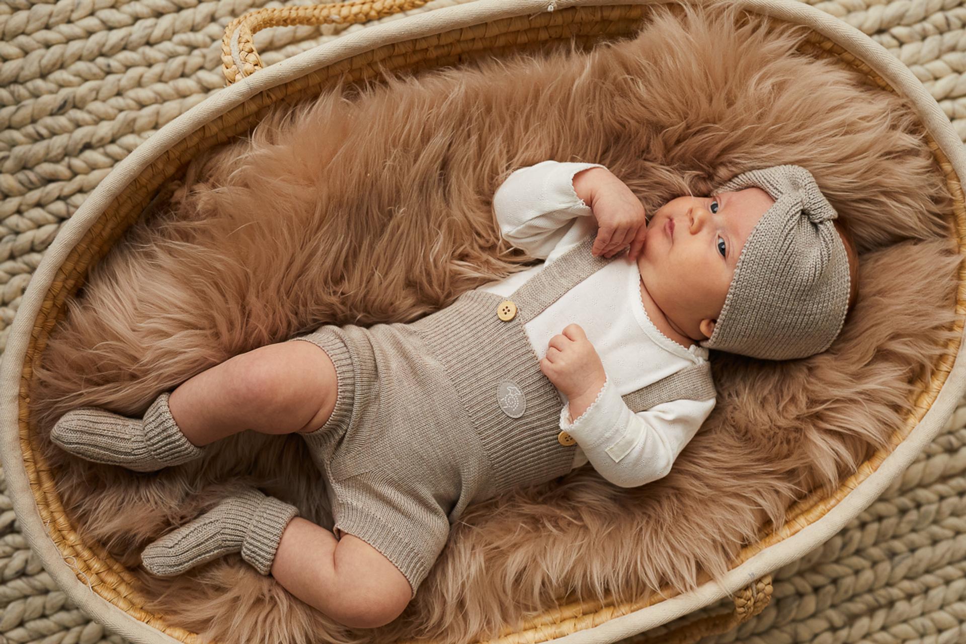 Baby in beige woolen clothes lying on a brown sheepskin