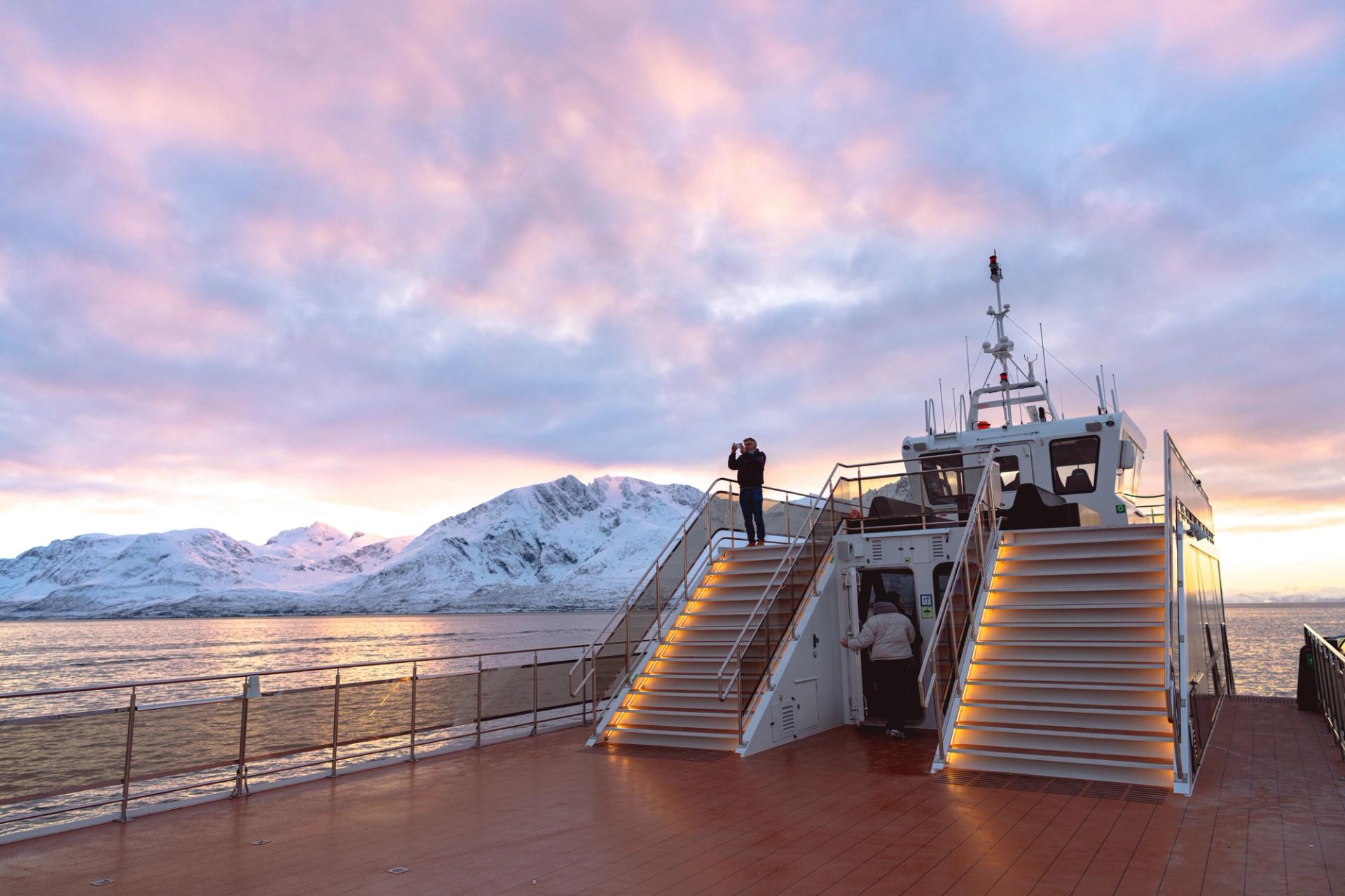 Man with binoculars on upper deck of Brim Explorer electric sightseeing catamaran at sunset