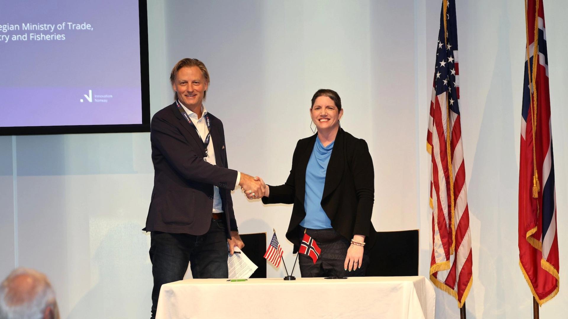 Man and woman shaking hands in front of an American flag and a Norwegian flag