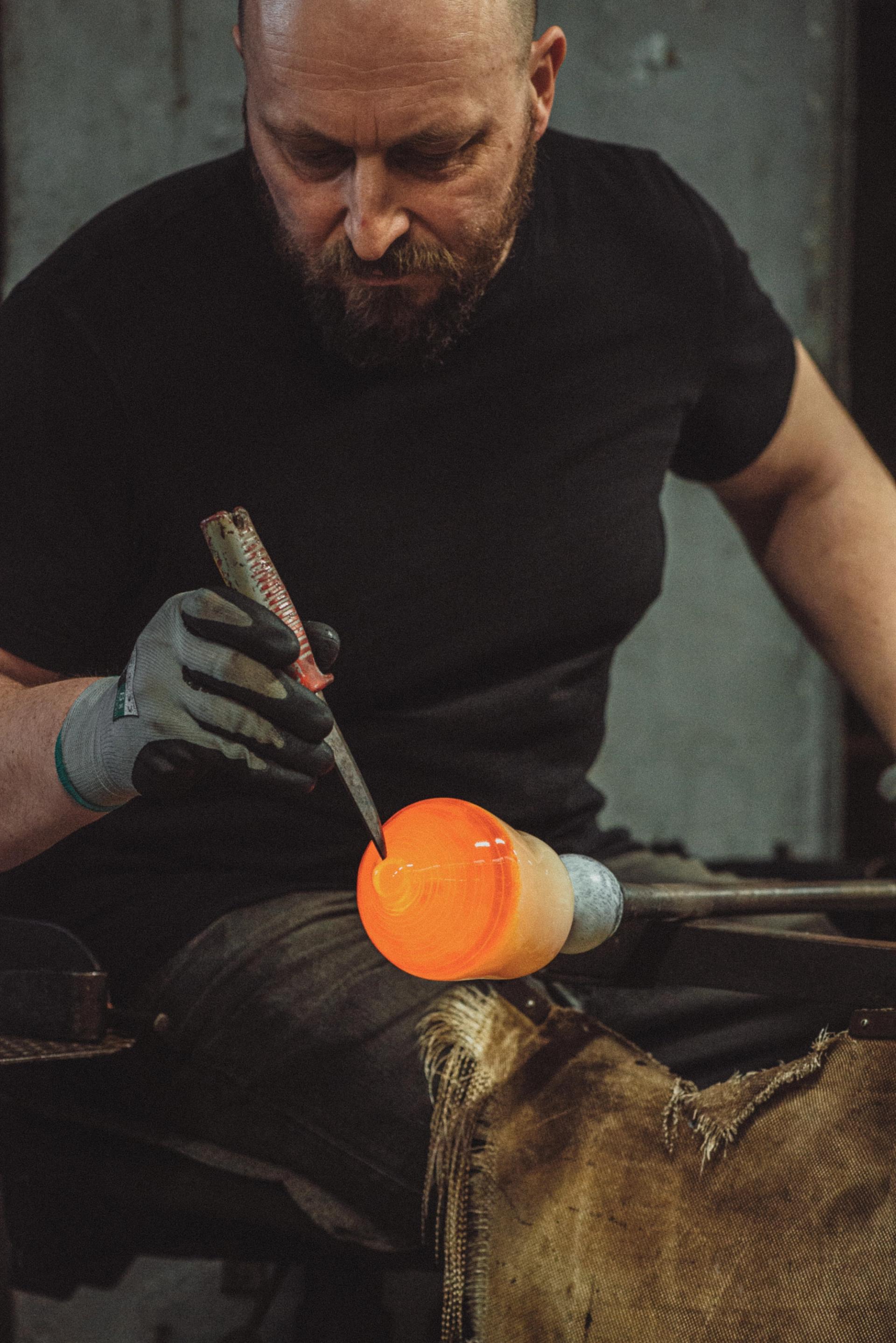 Man in a black t-shirt blowing orange glass