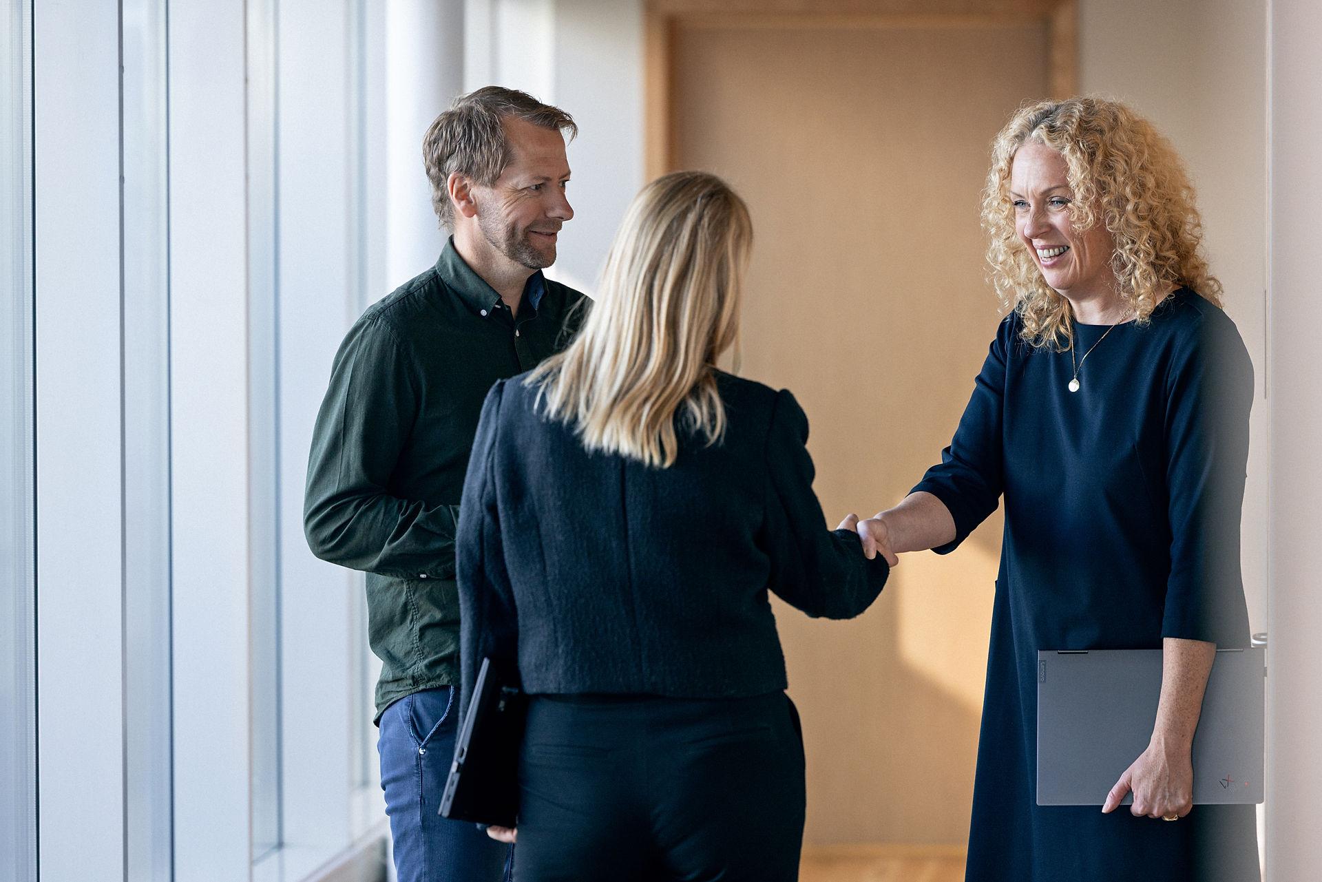 A woman with curly blond hair shaking the hand of a woman with straight blond hair while a blond man looks on