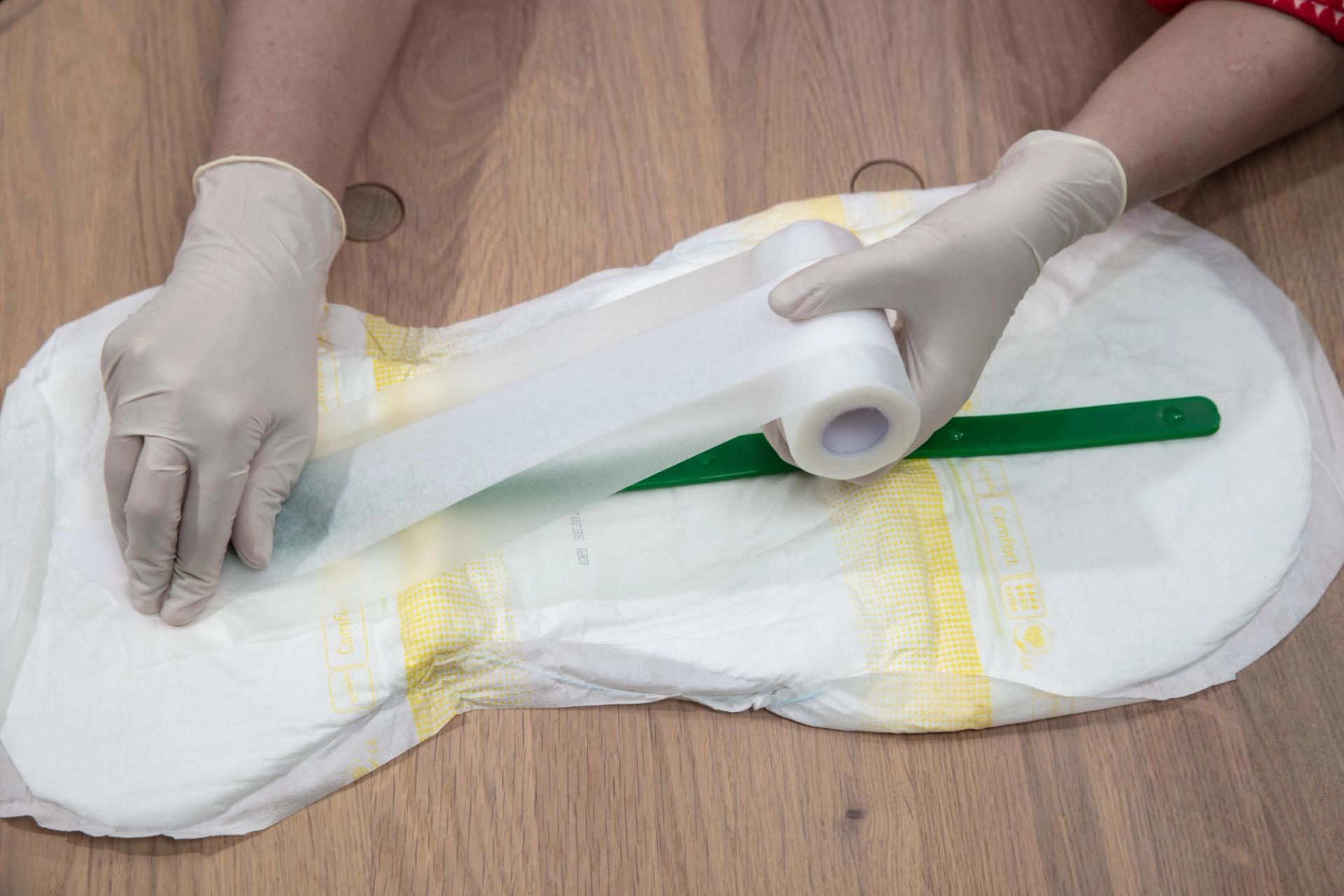 Person wearing gloves taping a dark green urine sensor onto an adult diaper