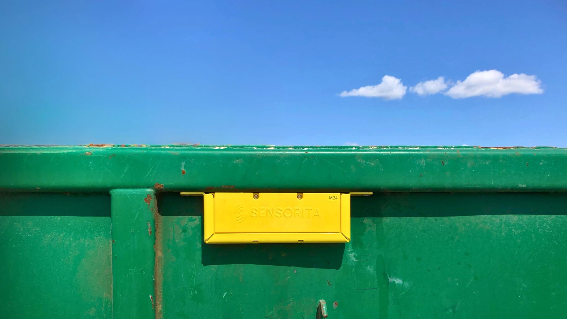 Yellow sensor box on the side of a green waste container