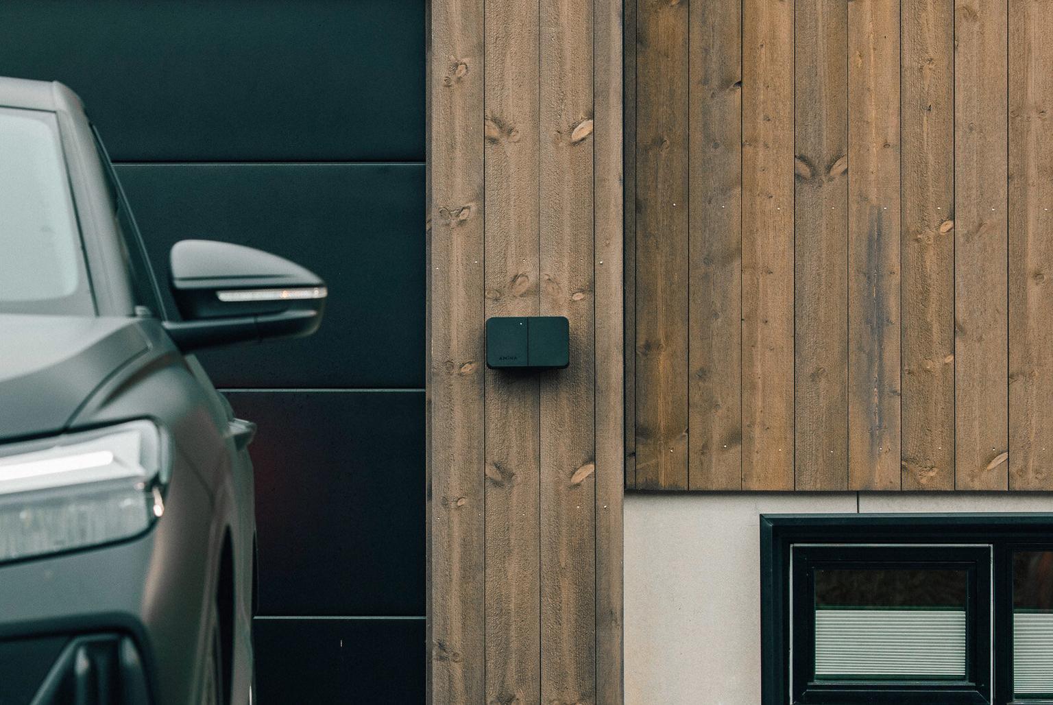 Black EV charger box on wooden wall next to a car