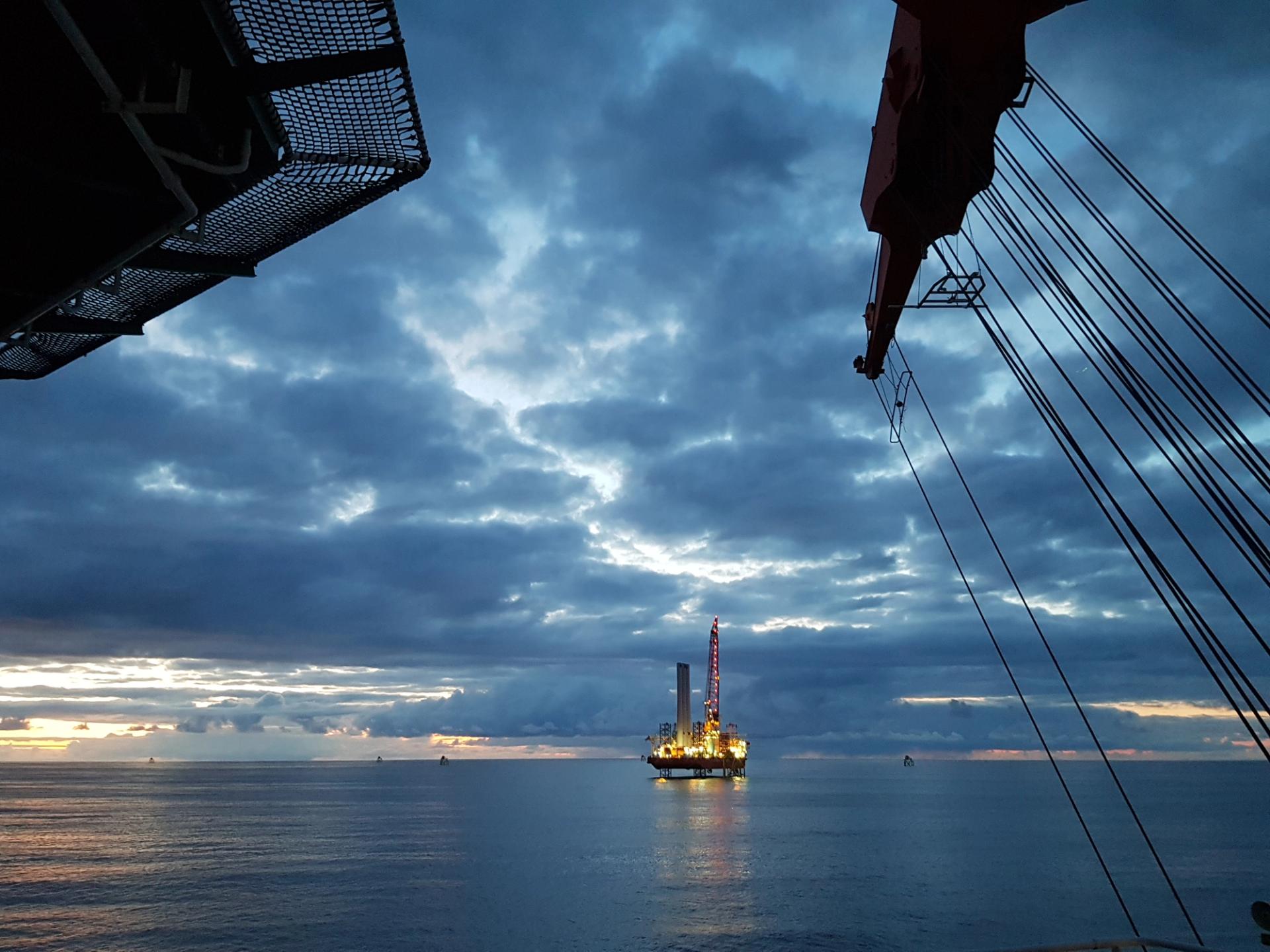 View of a lit-up jack-up vessel alongside an offshore wind turbine.