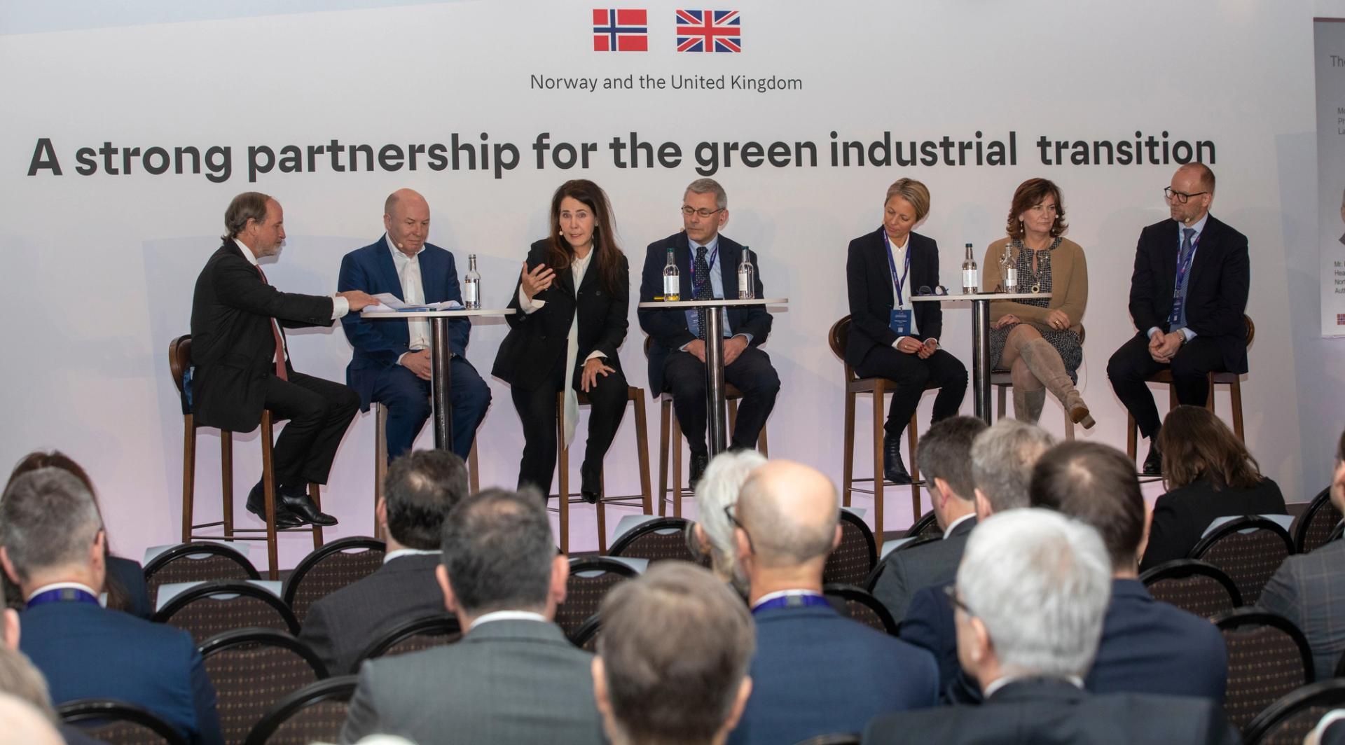 Group of people sitting at high tables with a sign behind them reading Norway and the United Kingdom - A strong pertnership for the green industrial transition