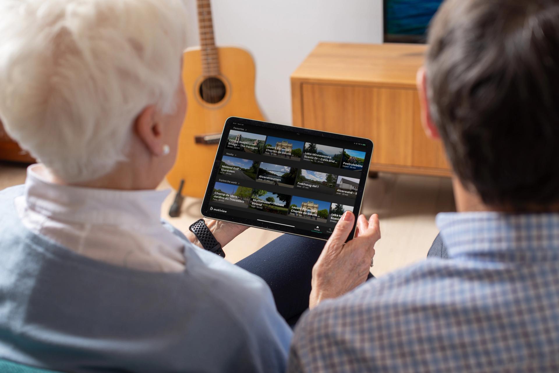 A grey haired woman choosing from a selection of videos on a tablet
