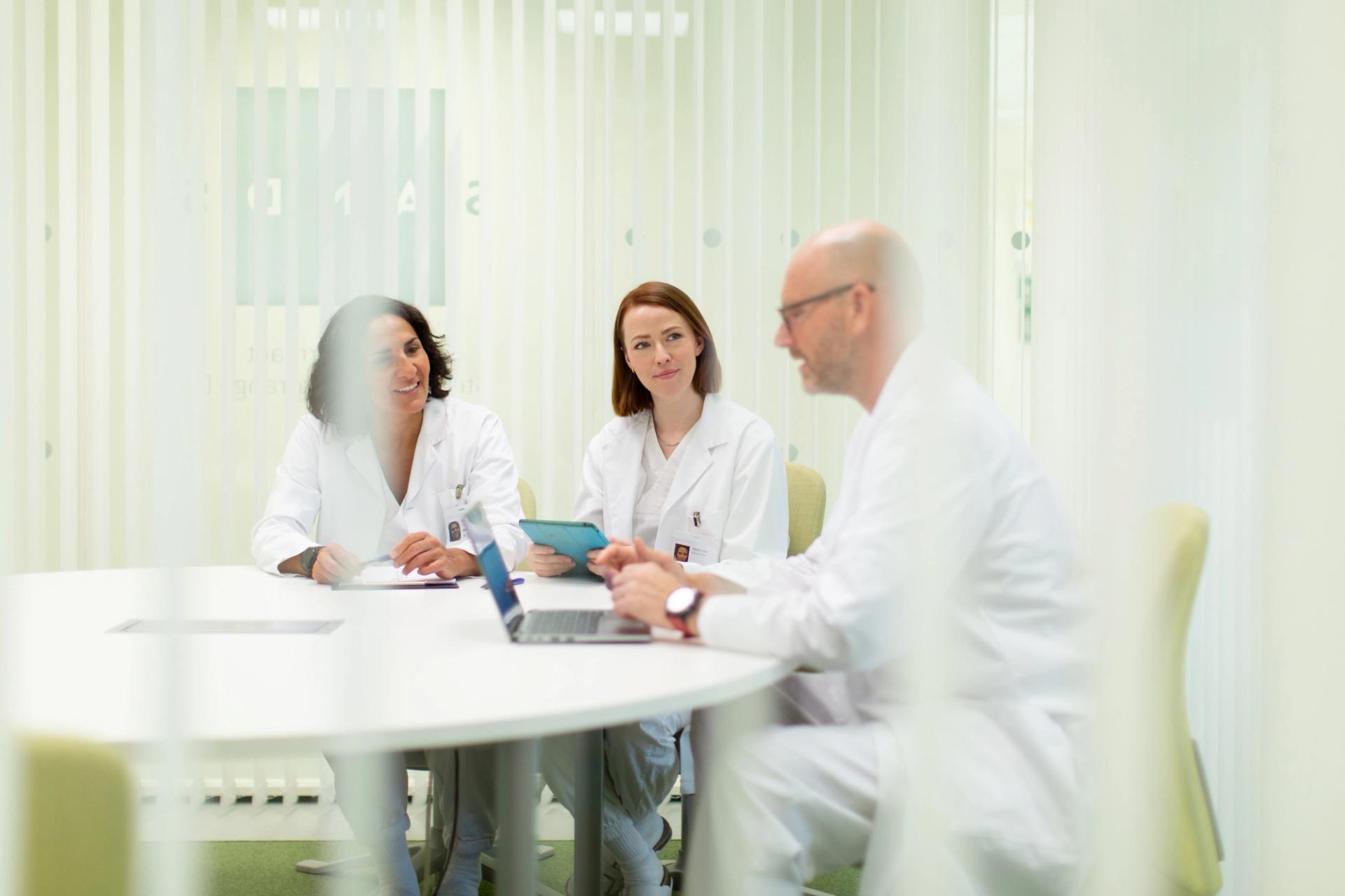 Two women and one man in white lab coats seated around a round white table