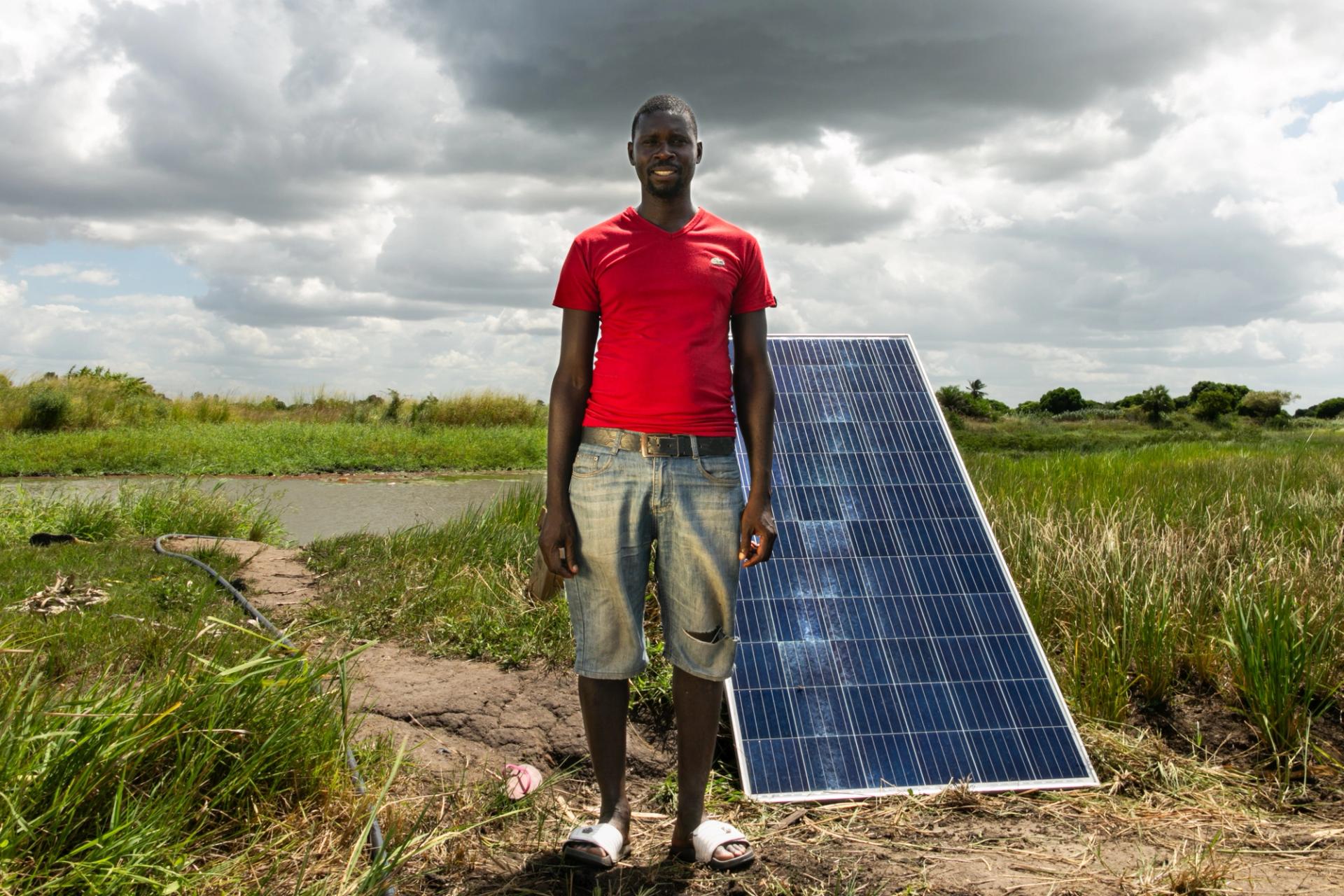 Man in red t shirt standing in front of a solar panel in a field