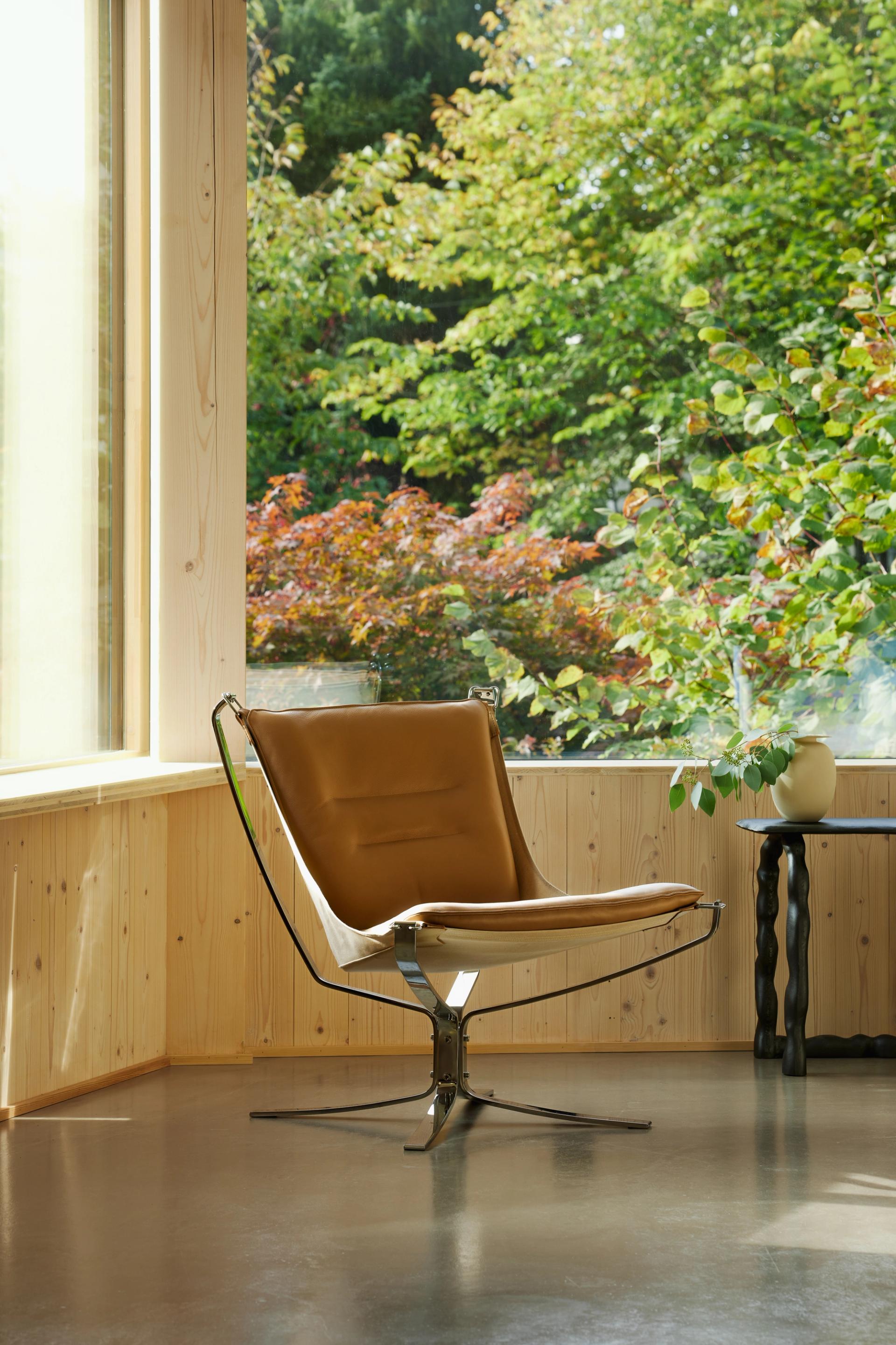 A brown chair in a living room with big windows.