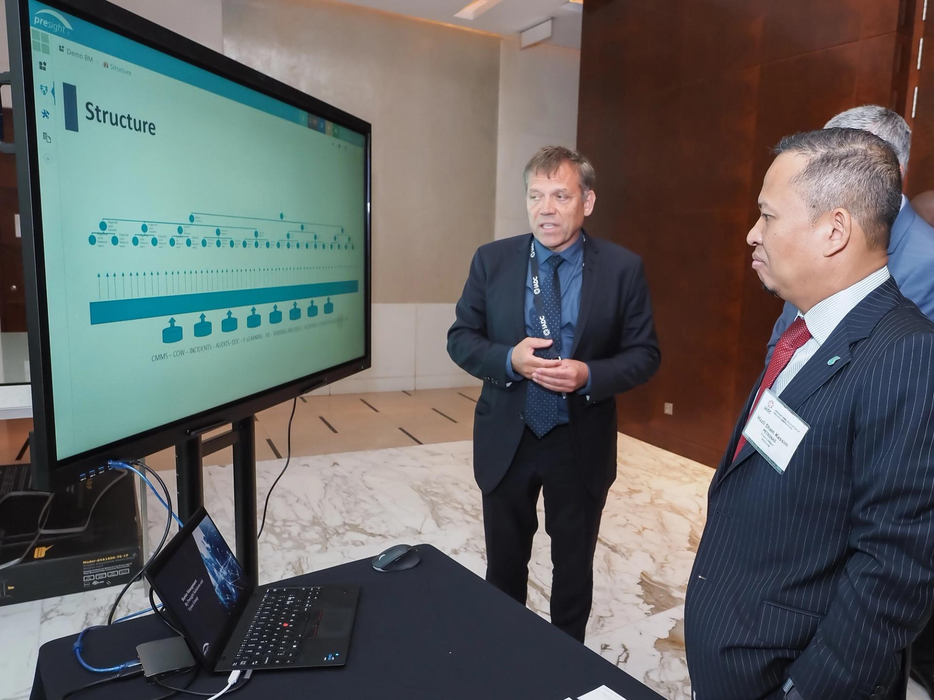 Three men in suits looks at a large computer screen on wheels