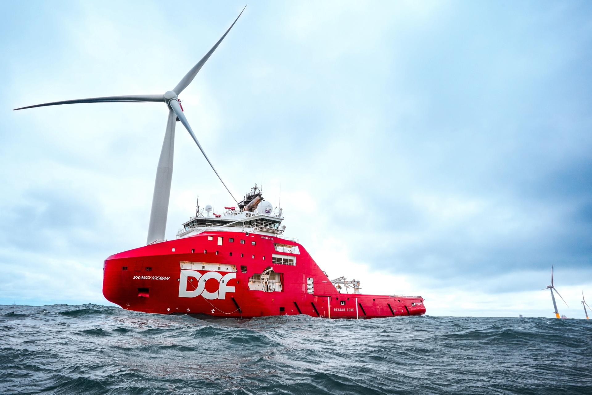 Red boat in front of a white offshore wind turbine