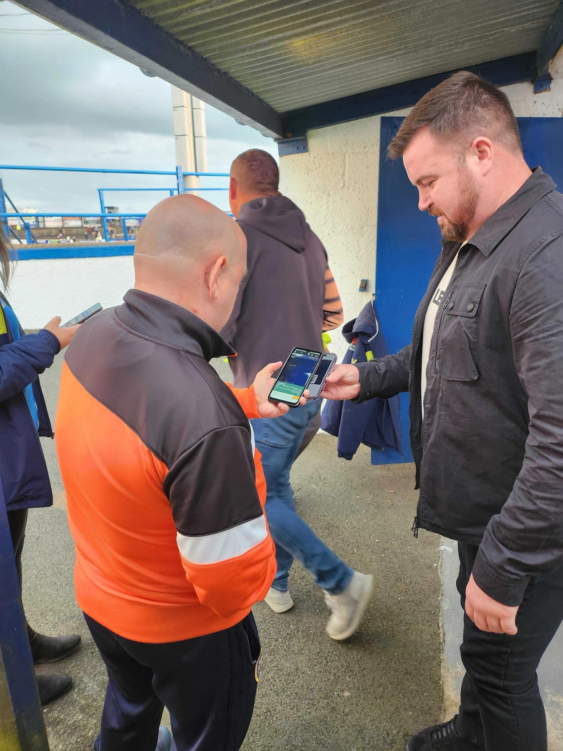 A man showing his ticket on his phone to get into a football match.