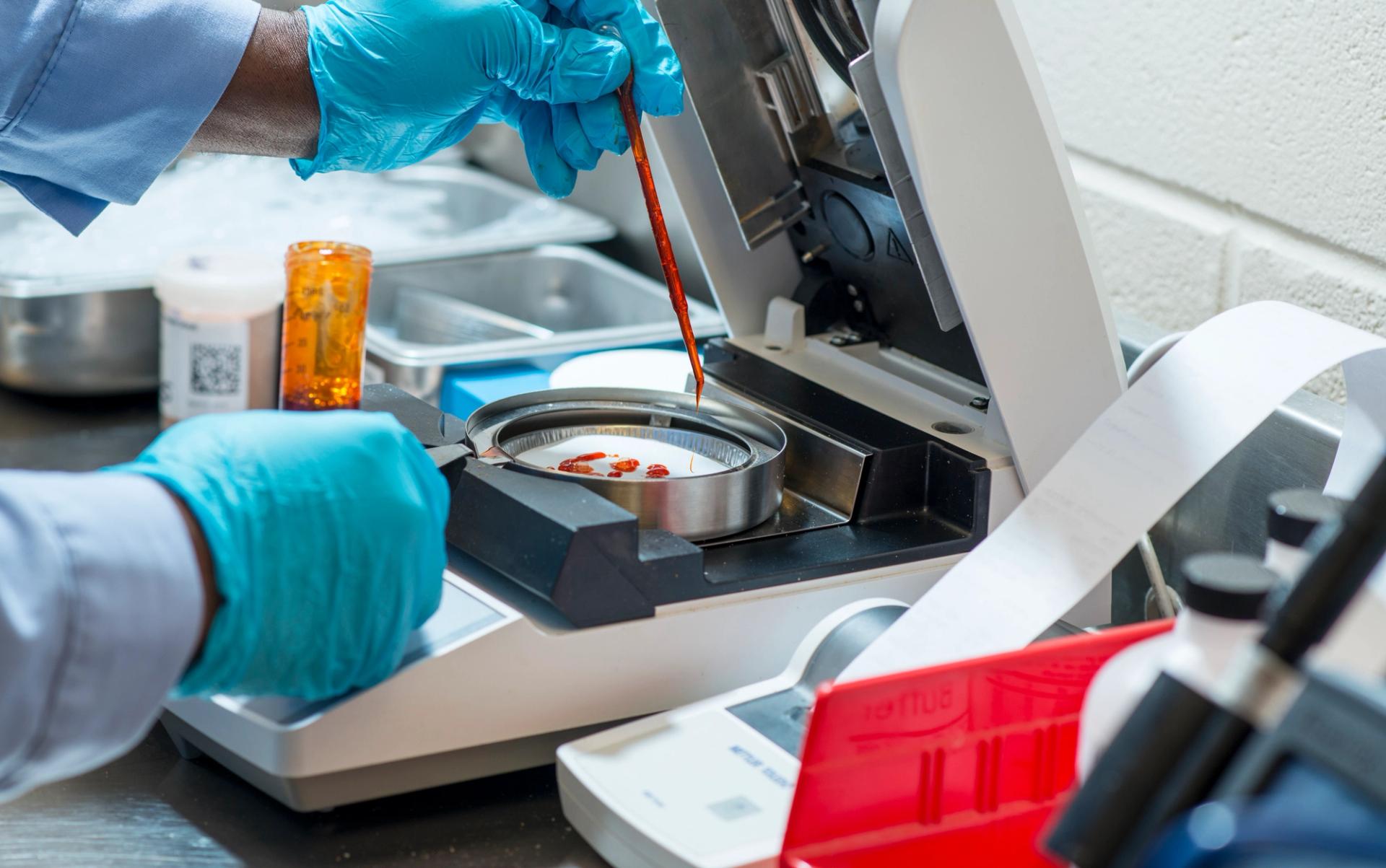 Person with blue gloves testing red liquid in a lab