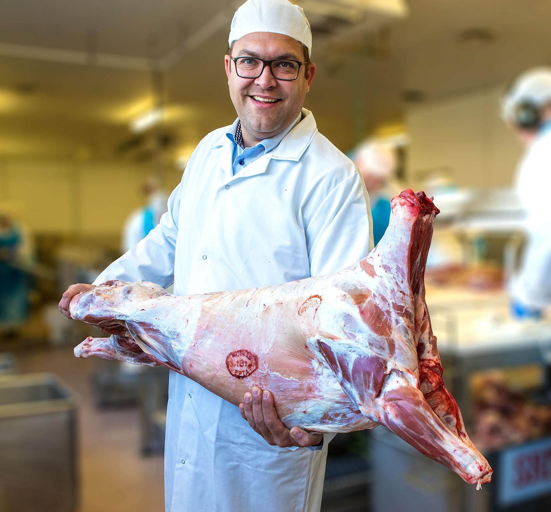 A butcher holding a peach of lamb meat.