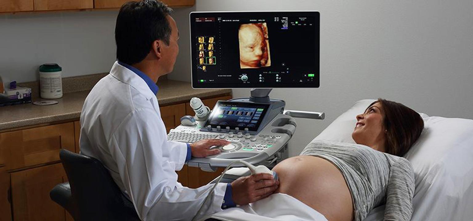 Doctor in white coat performing an ultrasound on a pregnant woman