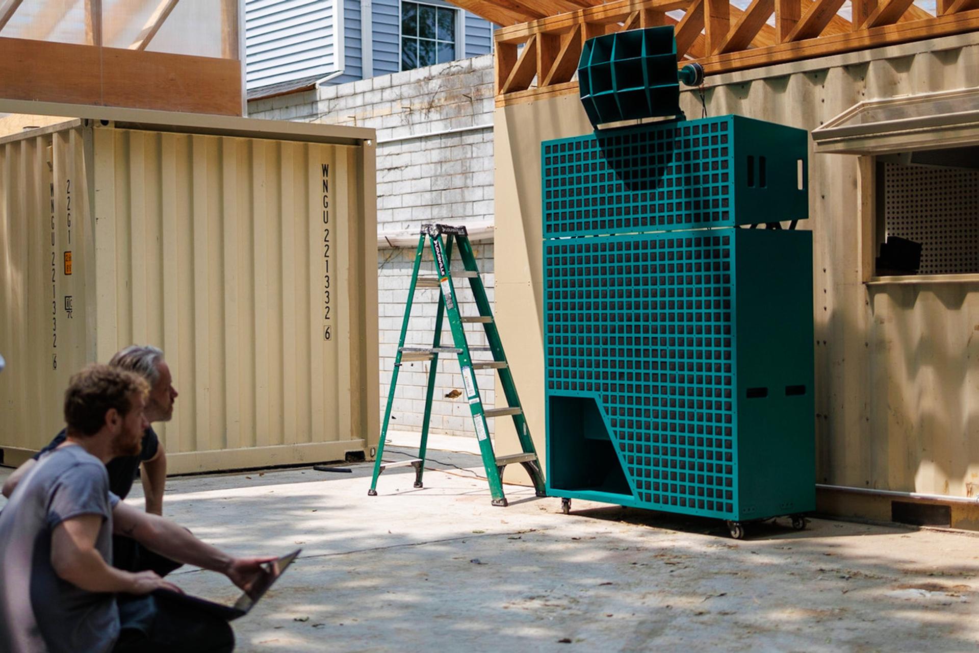 Giant green loudspeaker in front of a wooden building