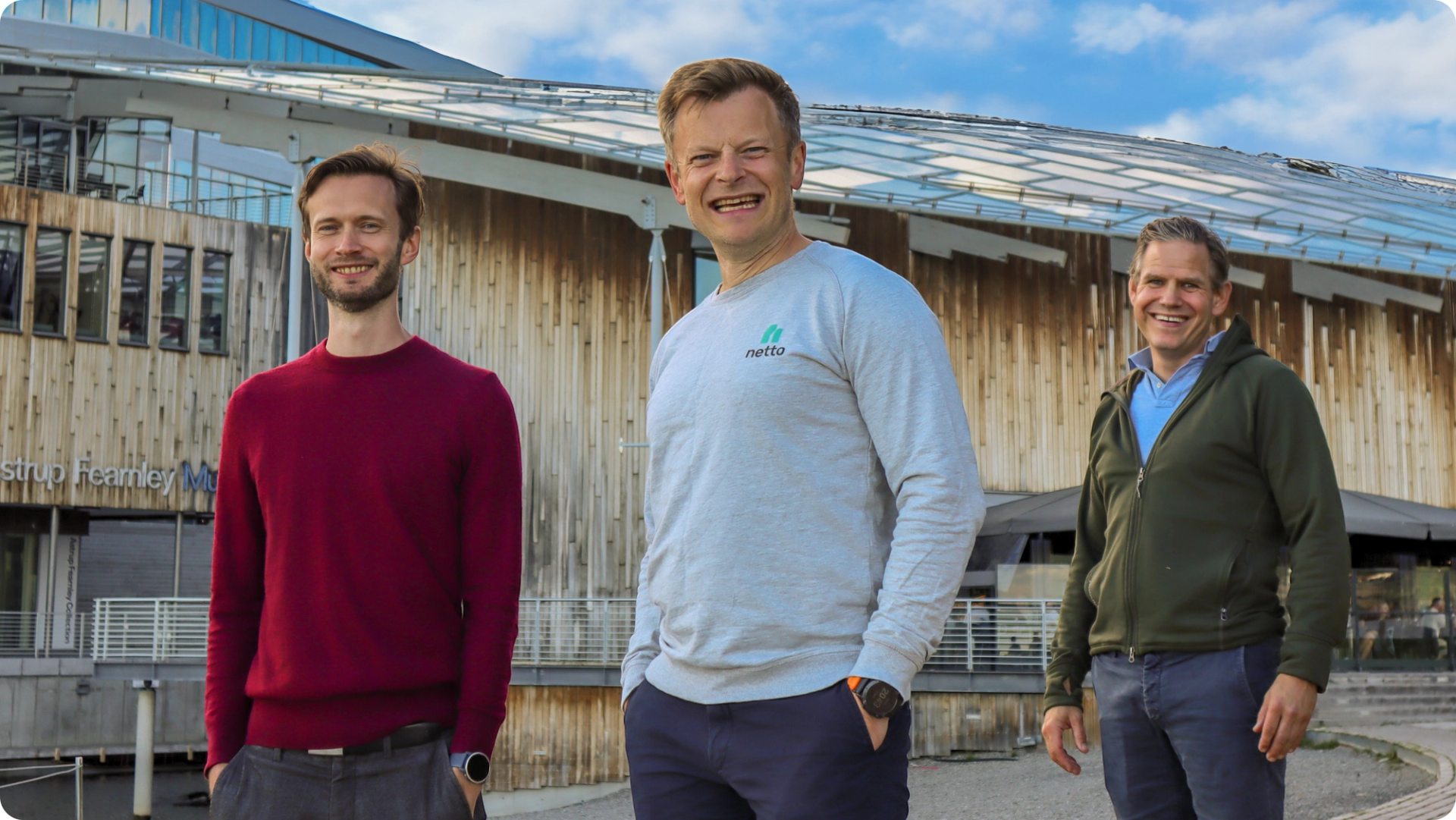 Three smiling men in sweatshirts in front of a modern art museum in Oslo, Norway