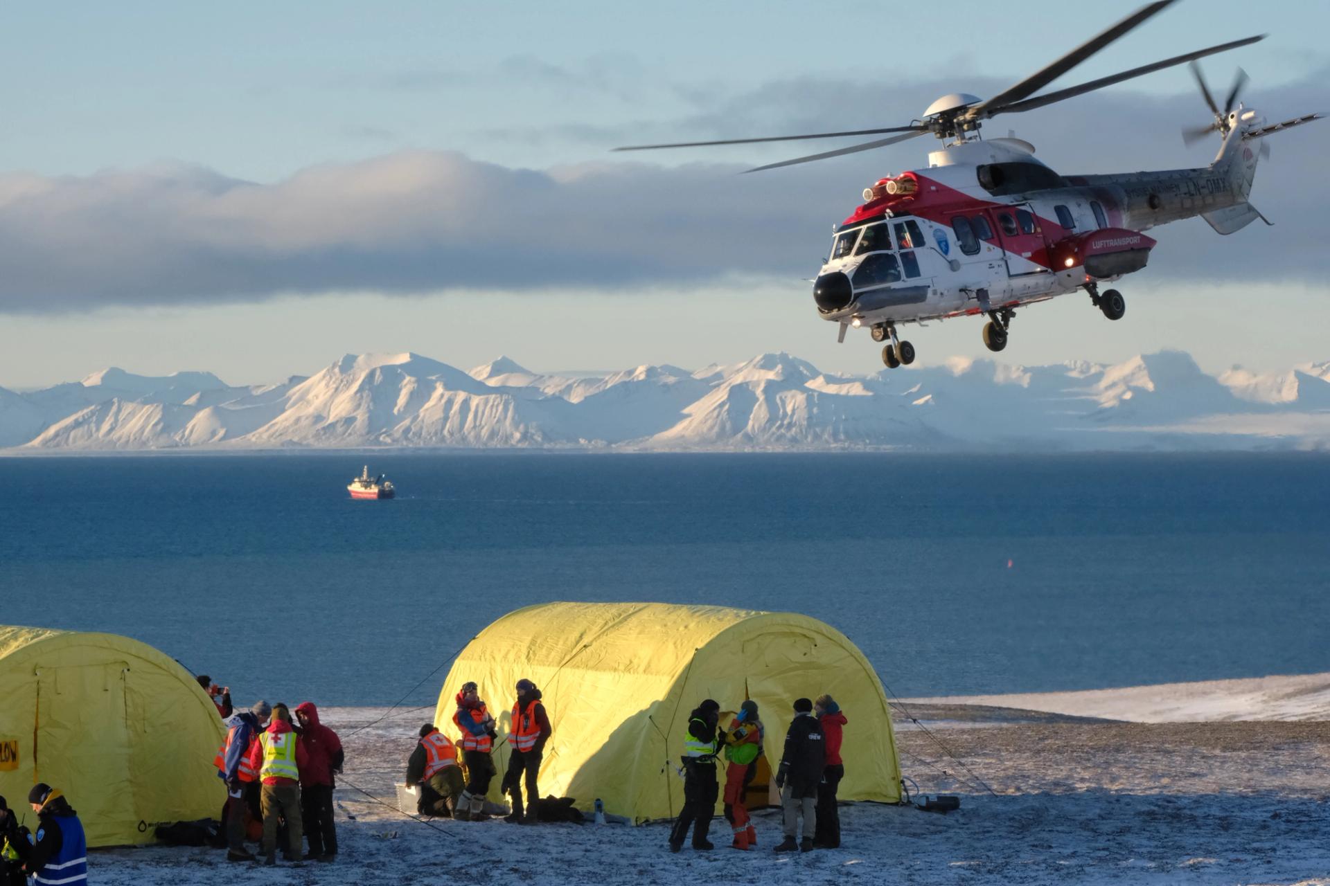 Helicopter coming in for landing besides yellow tents on Svalbard