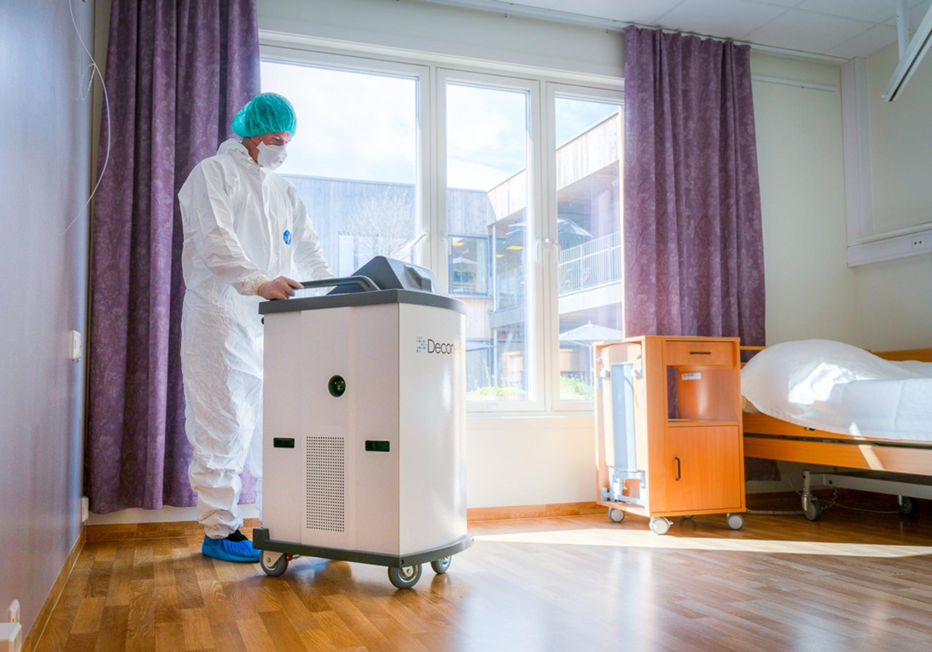 Person with infection control equipment rolling a machine in hospital room