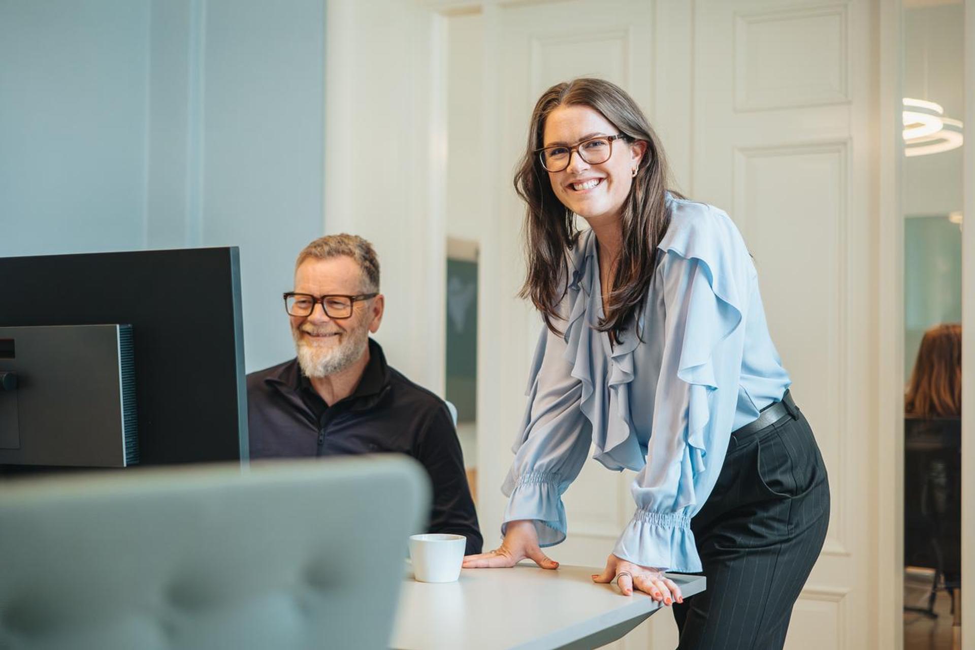 A girl and a man, two employees, smiling to the camera.