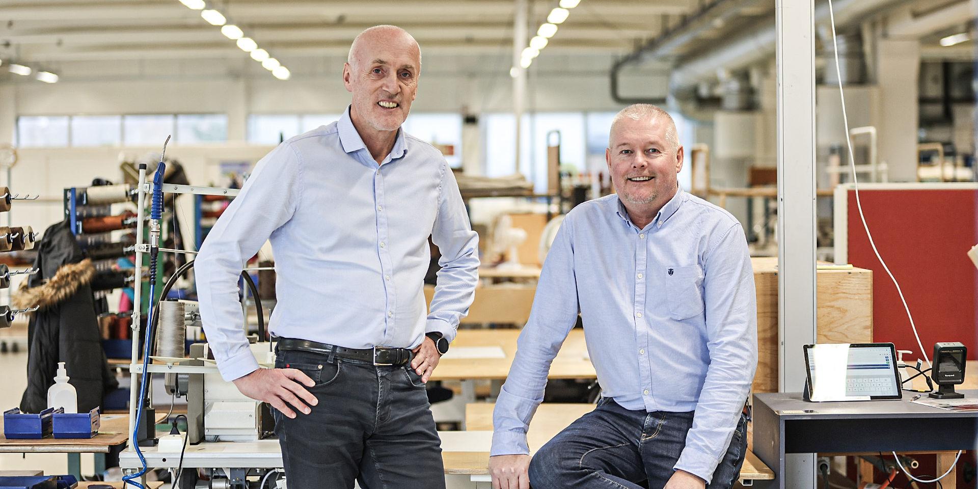 Two men in blue shirts smiling to the camera.