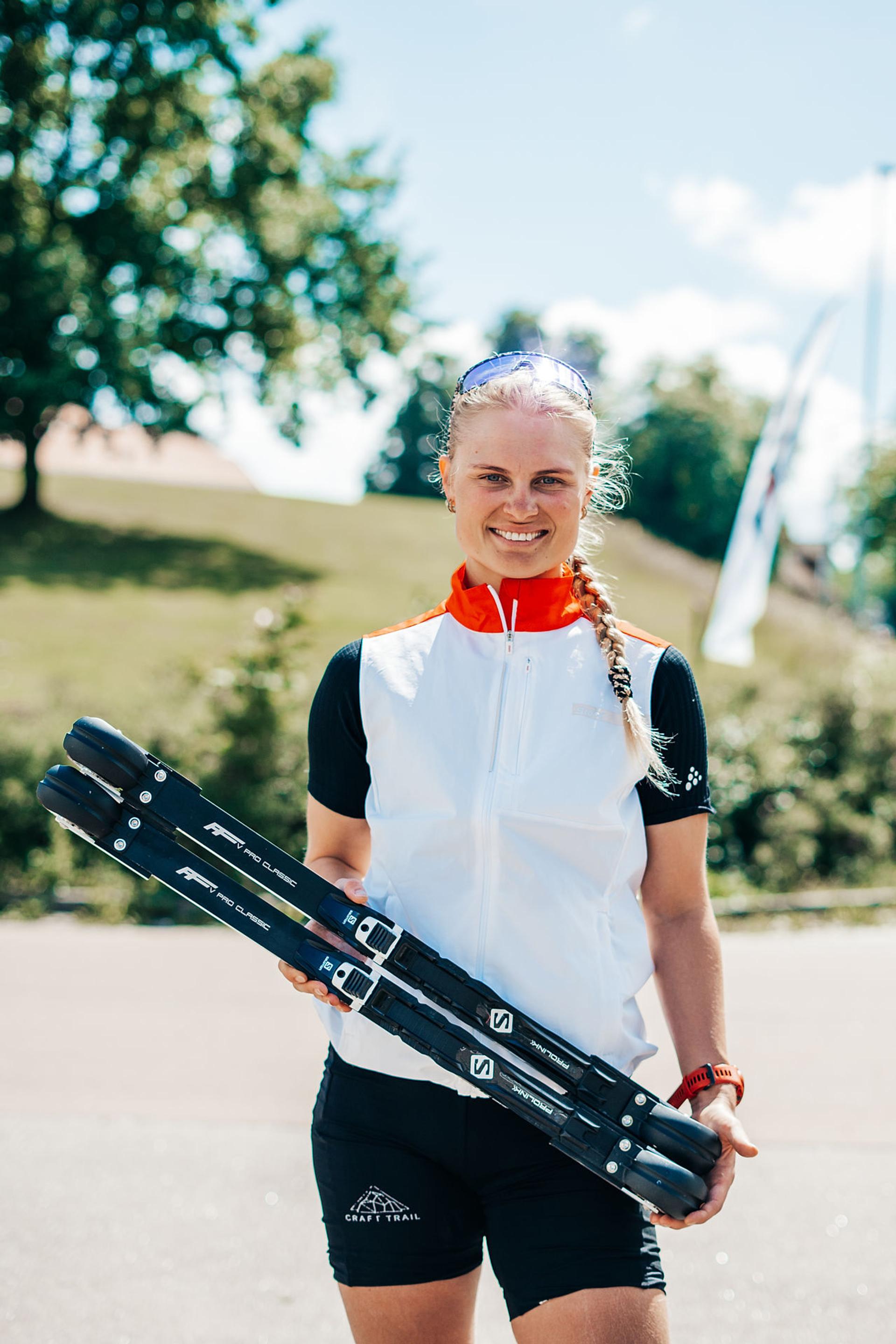 A girl holding her rollerskis and smiling to the camera.