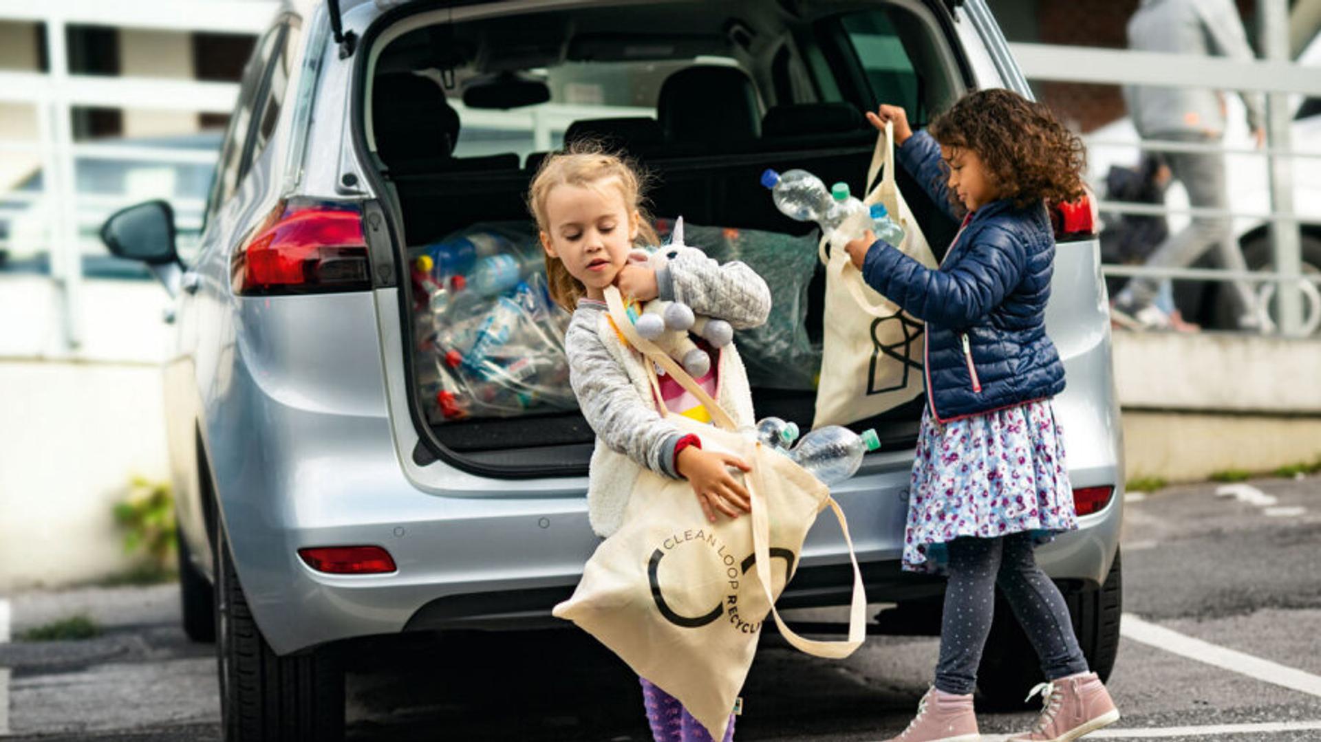 Little girls taking bags of empty bottles out of the back of a car