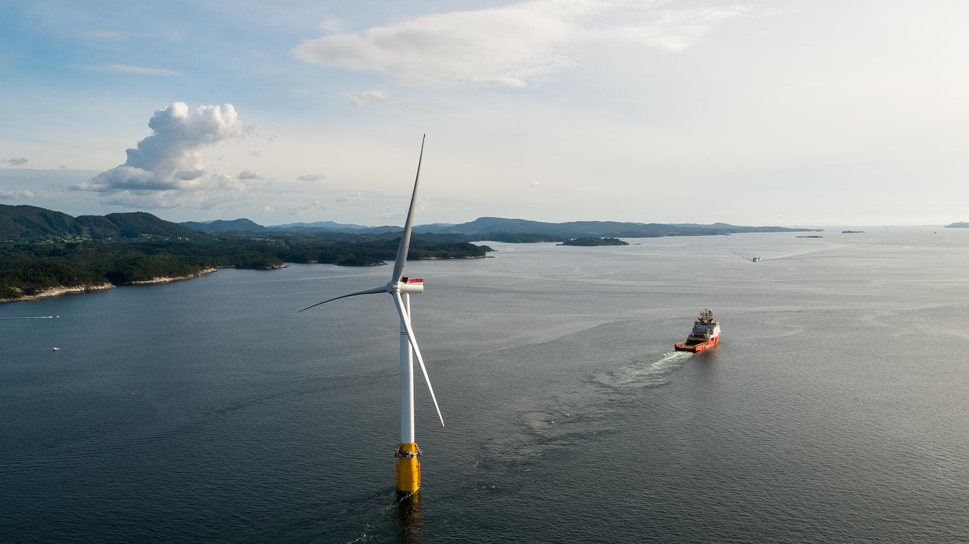 Wind turbine in coastal setting with offshore vessel in the distance