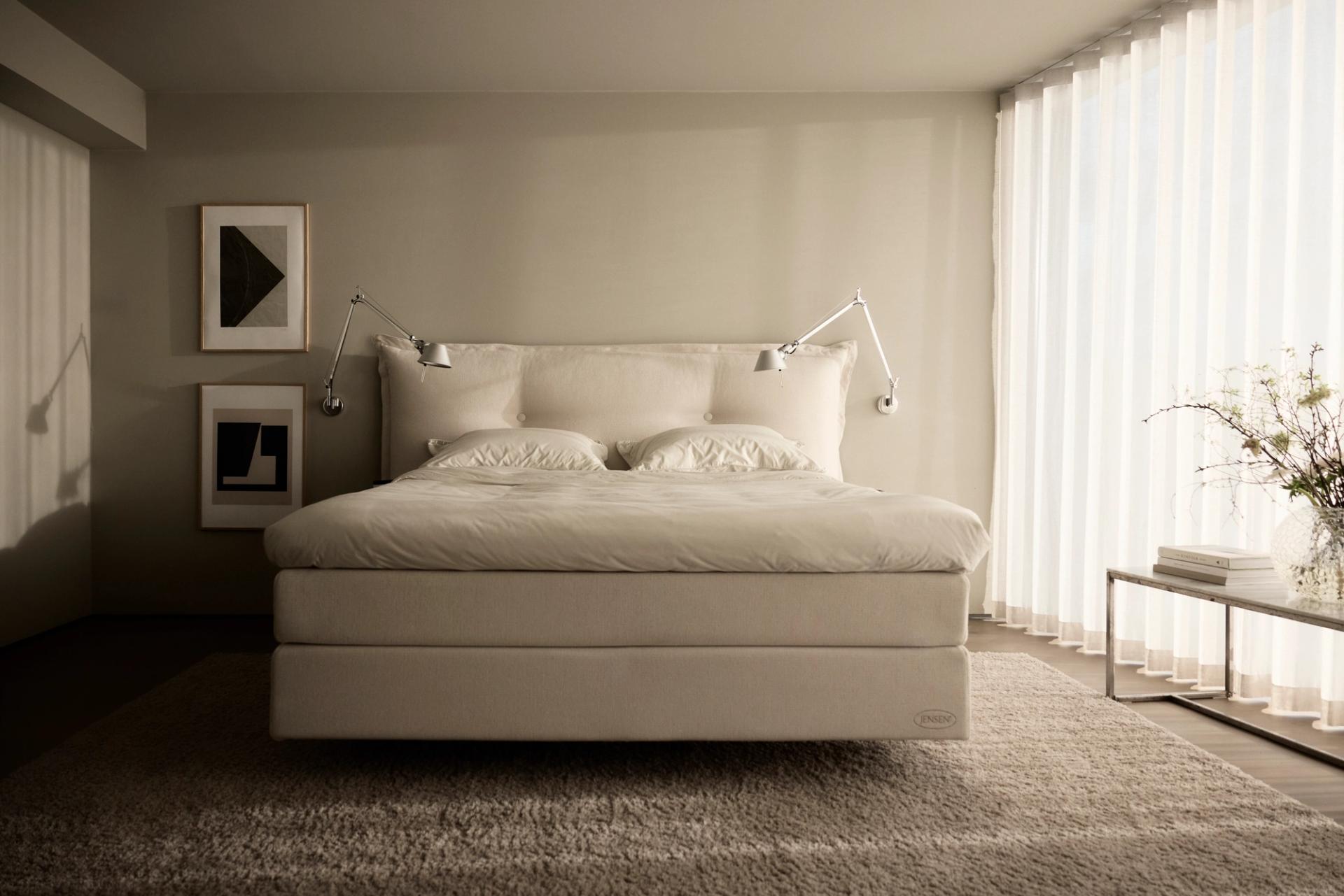 A bed in abide bedroom, with light shining through the windows.