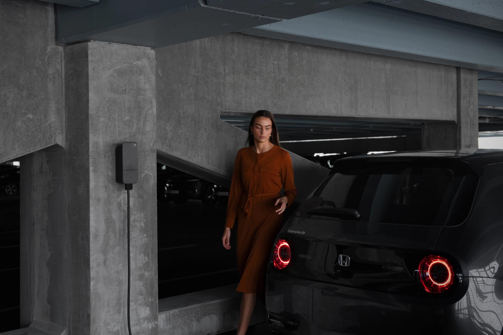 Woman walking past an electric car in front of a cement wall
